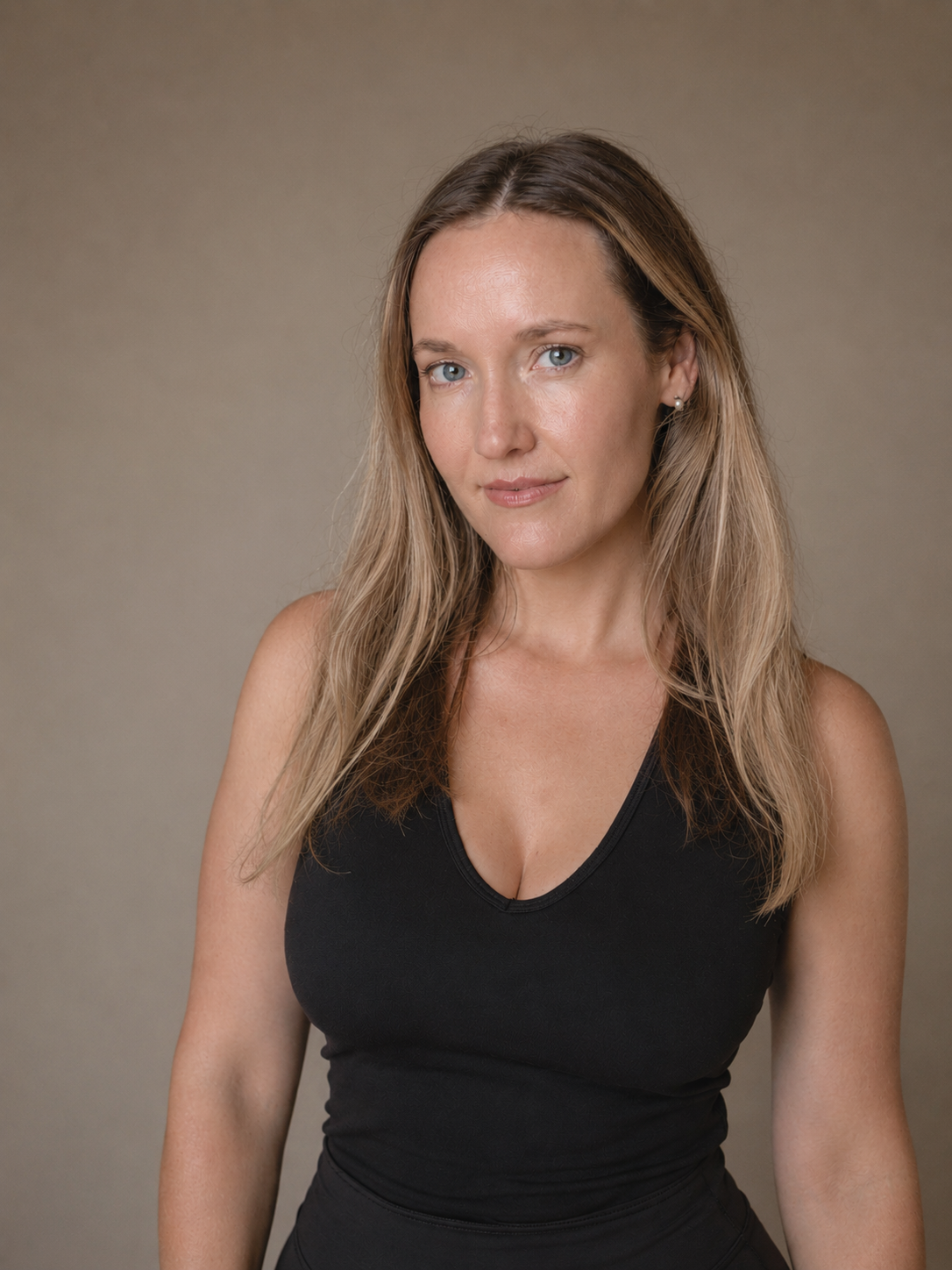 A woman with long blonde hair wearing a black sleeveless top, looking at the camera with a slight smile, against a neutral background.