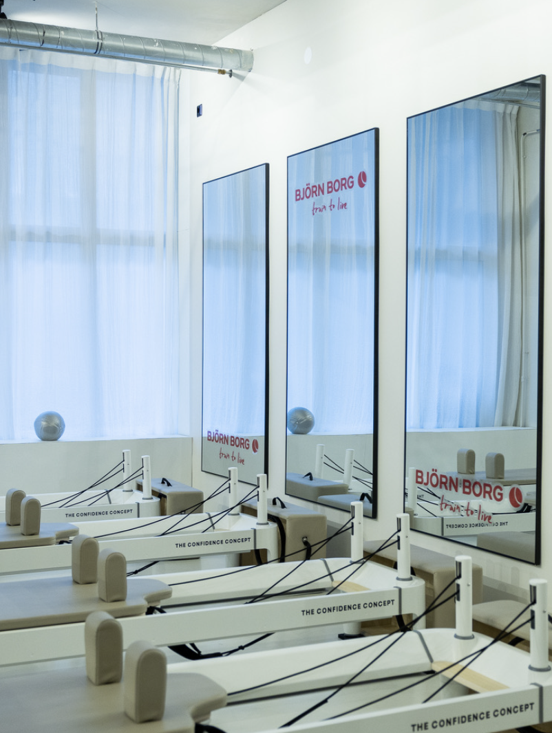 Row of Pilates reformer machines in a studio with mirrors on the wall and Björn Borg advertisement posters.