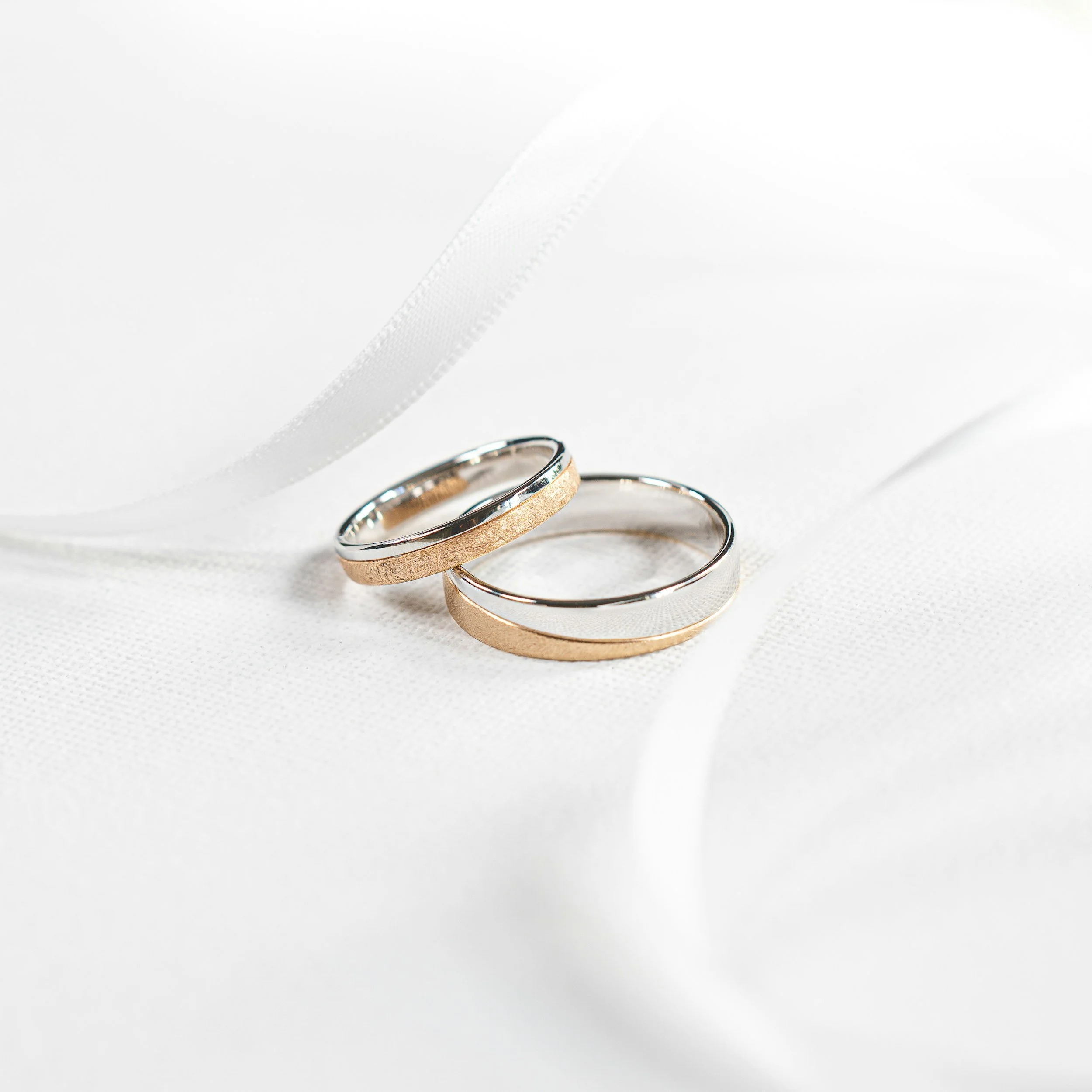 Close-up of three wedding rings with different textures and finishes resting on a white surface.