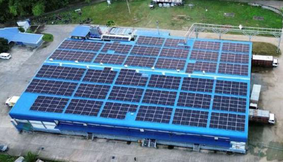 Large building with many solar panels on the roof, surrounded by trees and a parking lot.