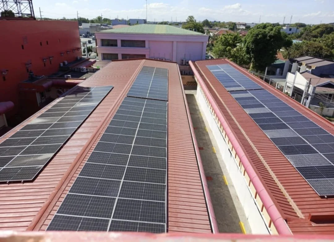 Two rooftops with solar panels installed in an urban area, with buildings and trees in the background.