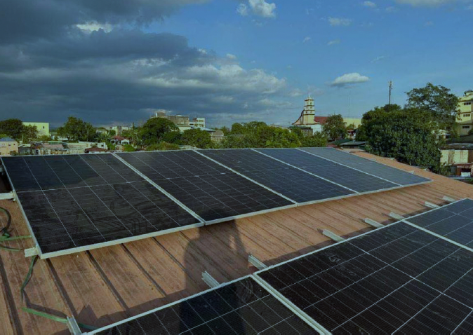 Multiple solar panels installed on a rooftop with a cityscape background, under a partly cloudy sky.