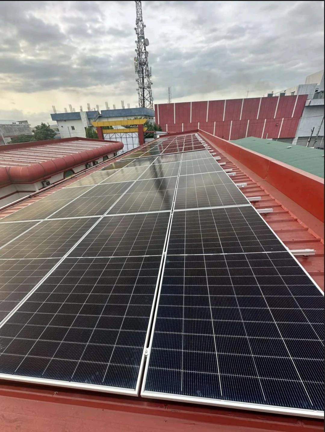 Solar panels installed on a red rooftop with cloudy sky in the background.