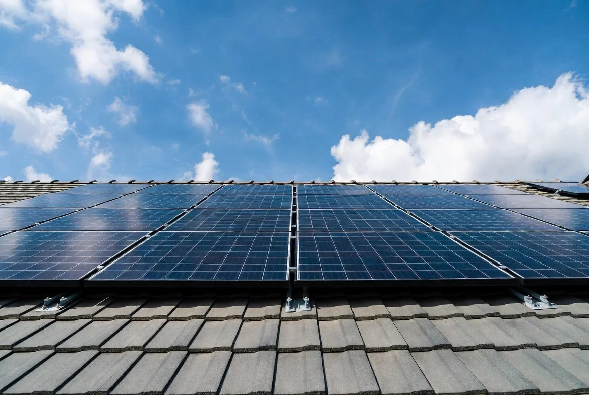 Solar panels installed on a house roof under a blue sky with clouds.