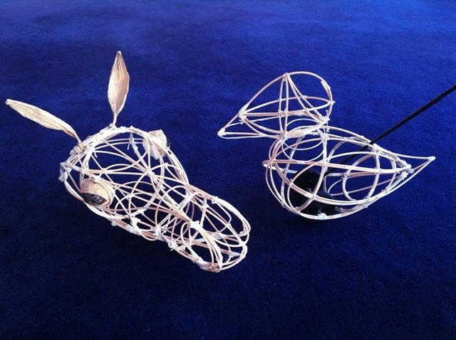 Two woven wicker animal sculptures on a dark blue surface, one resembling a rabbit and the other a bird.