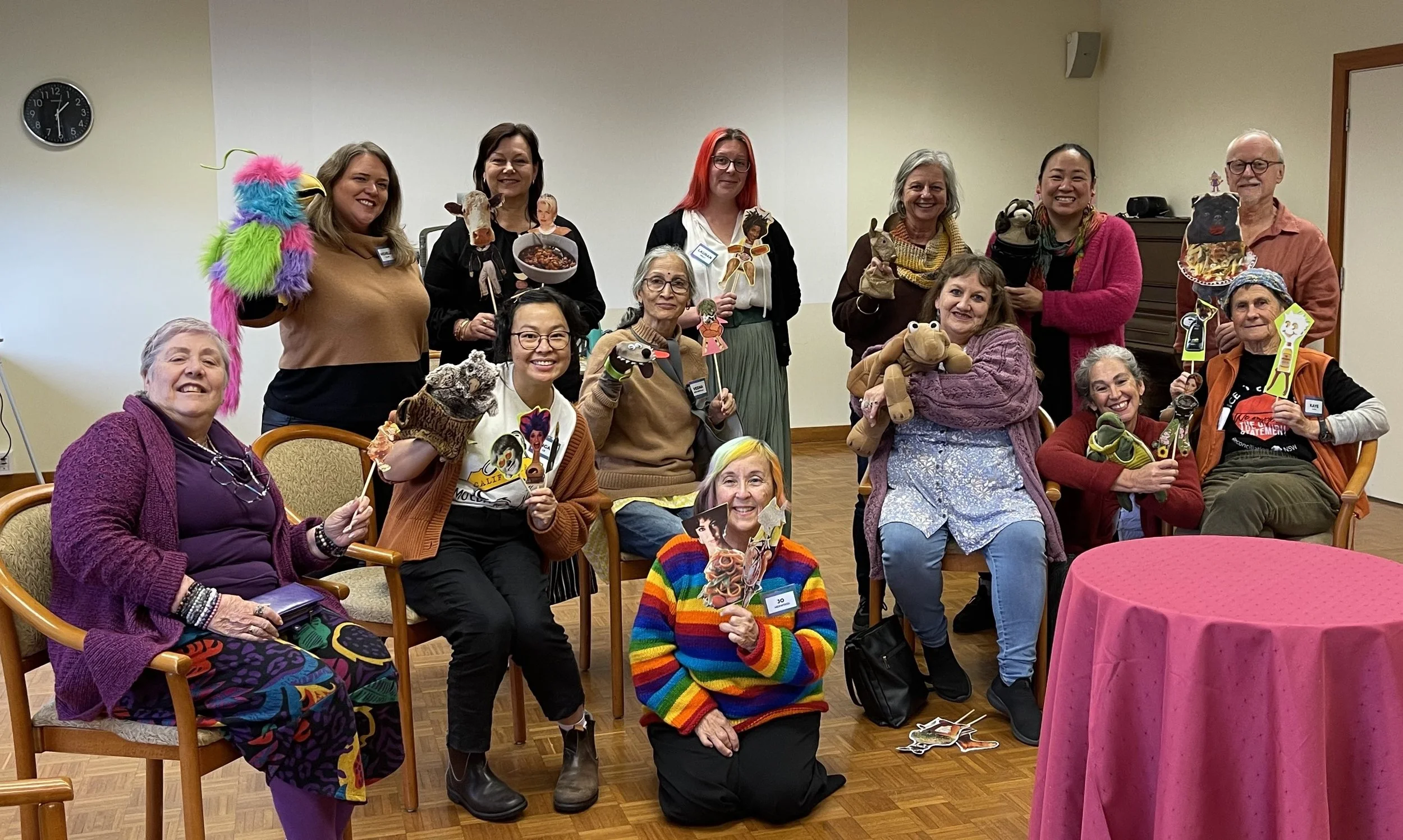 Group of people at an indoor gathering, some holding puppets or props, smiling and posing for a photograph.