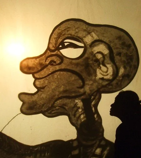 Silhouette of a person looking at a large cartoonish black and white mural of a distorted face with exaggerated features.