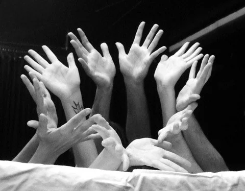 Multiple hands reaching upward in a black-and-white photo.