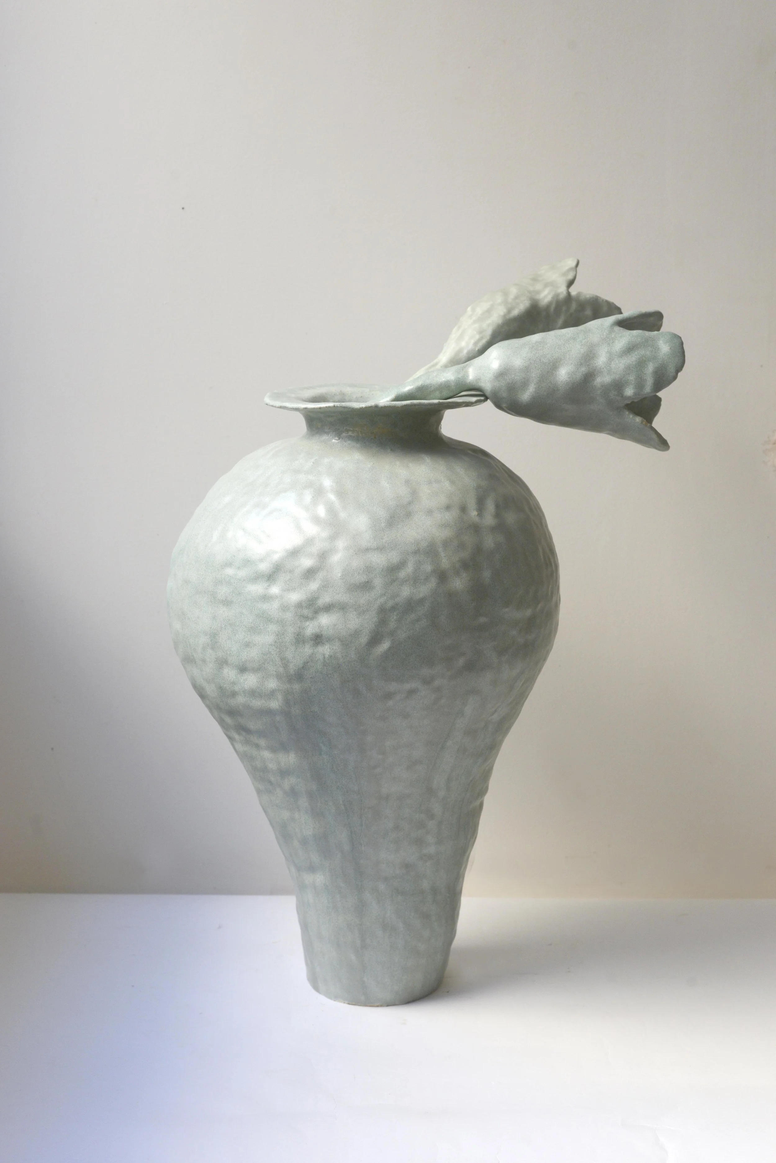 Une sculpture en céramique blanche représentant un vase avec des formes abstraites et organiques sur le dessus, avec une surface texturée