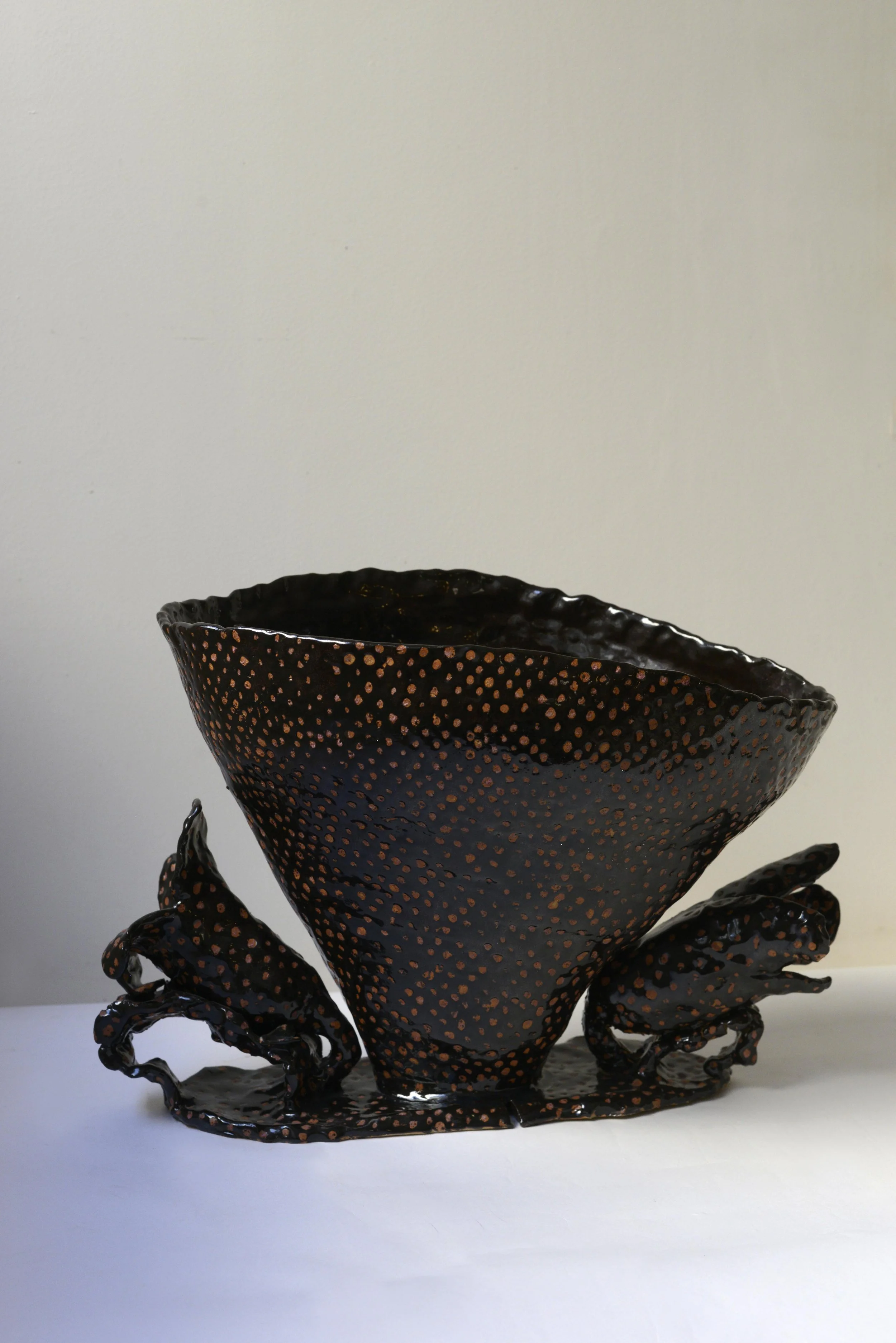 Une sculpture en métal représentant une crevette ou un crabe avec des détails perforés et des pattes torsadées, posée sur une surface blanche.
