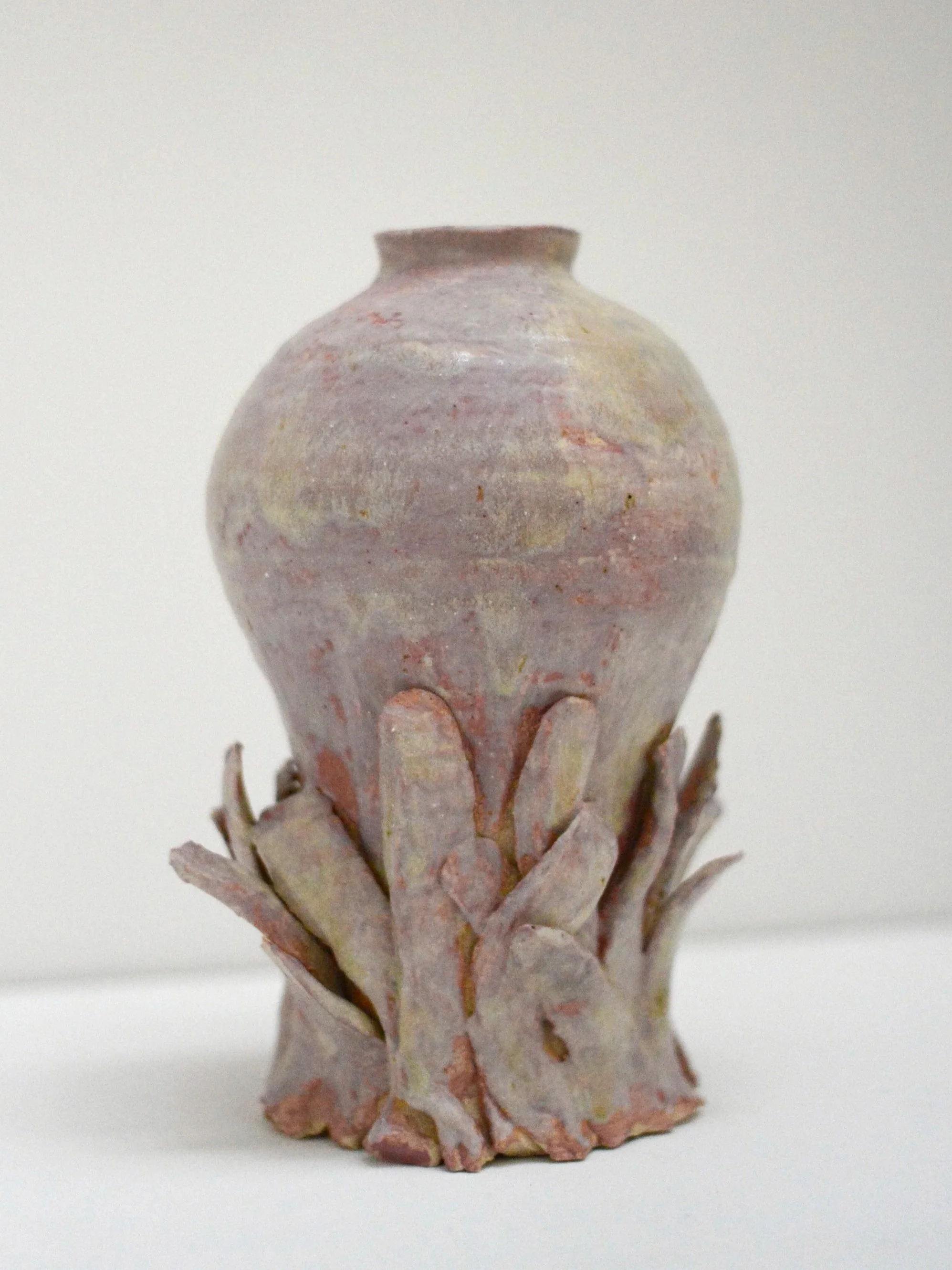 Vase en céramique avec un motif en forme d'écailles ou de feuilles, de couleur pastel beige, rosée avec des touches de jaune, positionné sur un fond blanc.