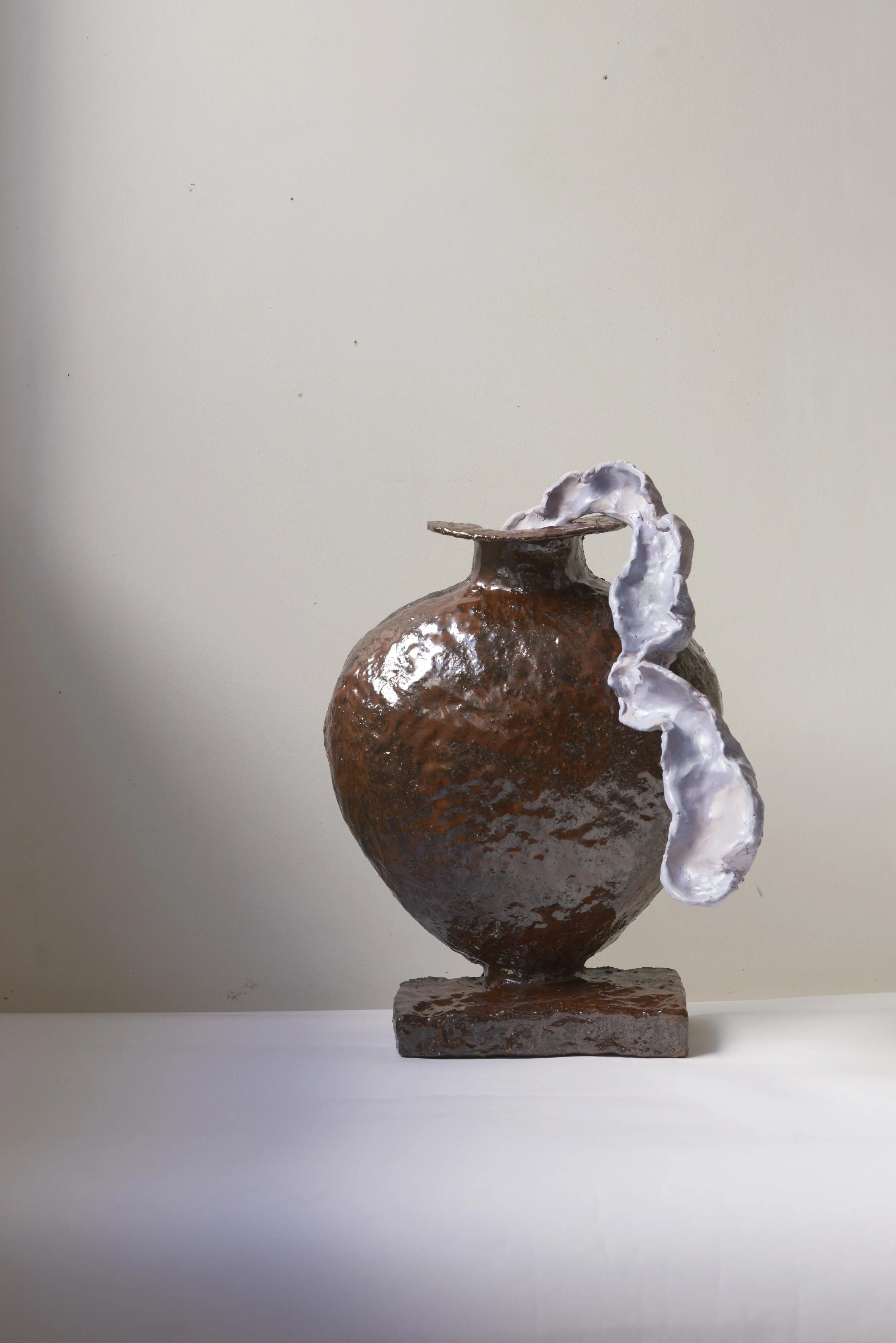 Une sculpture en céramique représentant un vase brun avec une texture rugueuse, ornée d'une branche blanche en relief qui s'enroule autour du vase, posée sur un socle rectangulaire en céramique.