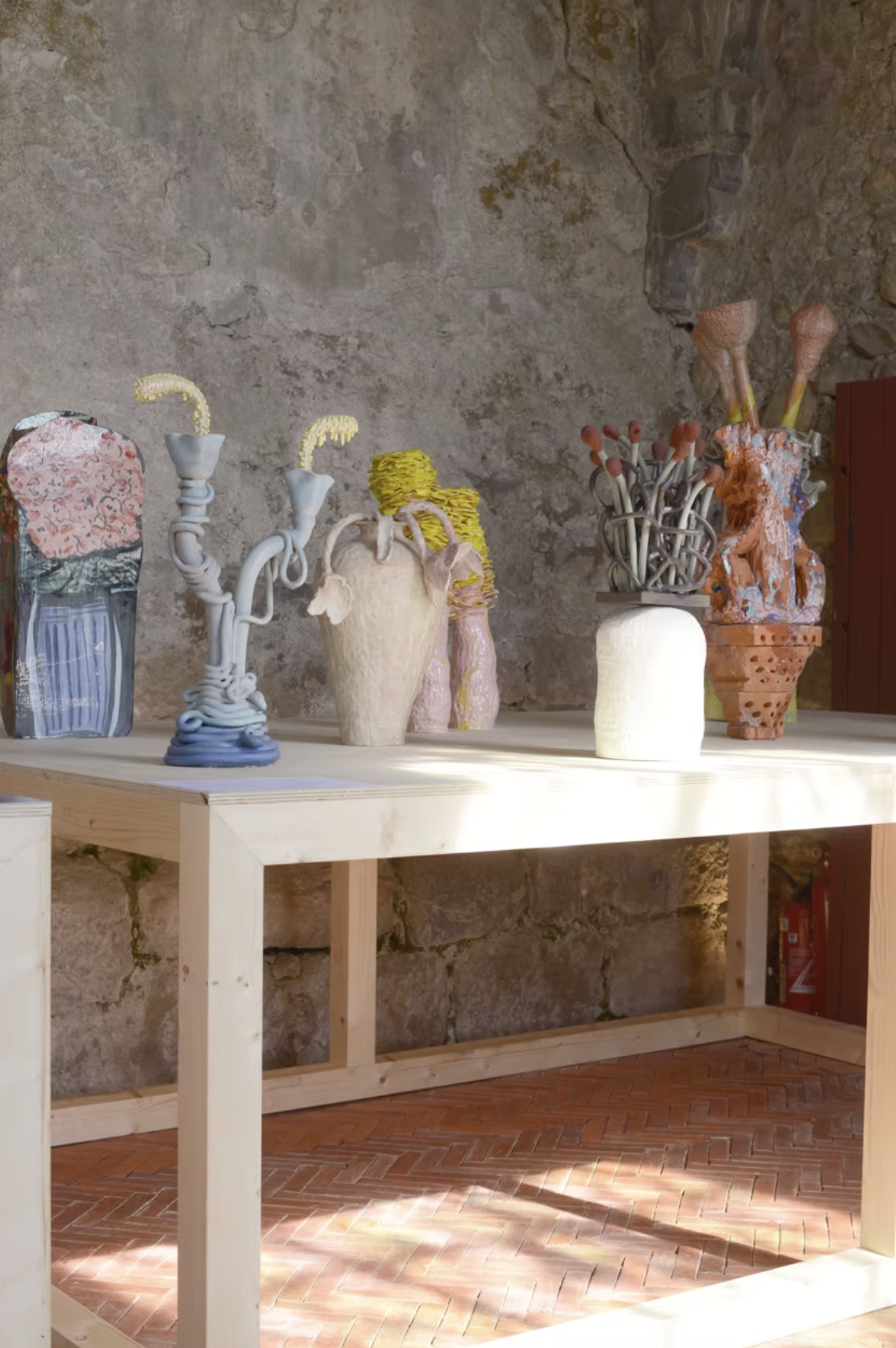 Vases artistiques colorés avec formes organiques en céramique sur une table en bois, fond en pierre