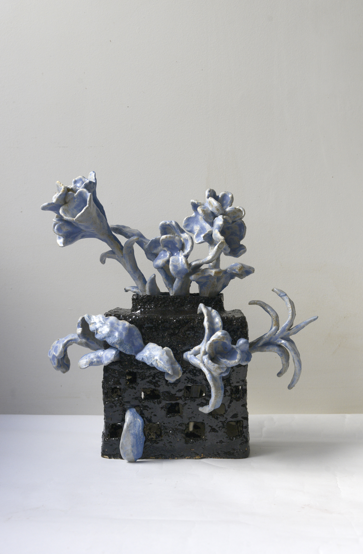 Une sculpture moderne représentant des formes florales bleues et blanches sur une base noire en relief, exposée sur une plateforme blanche contre un mur blanc.