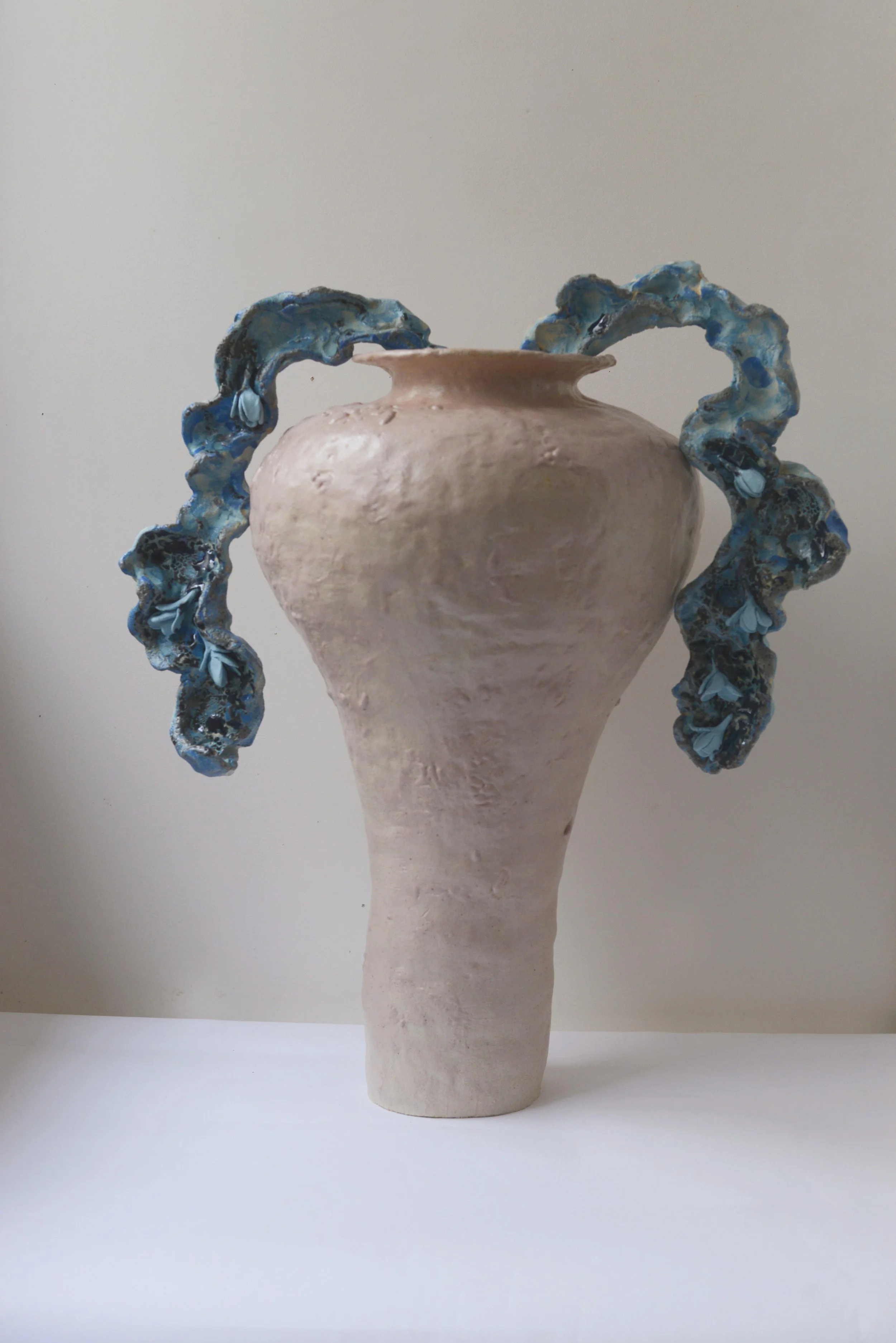 Vase en céramique beige avec anses en forme de vagues bleues et noires.