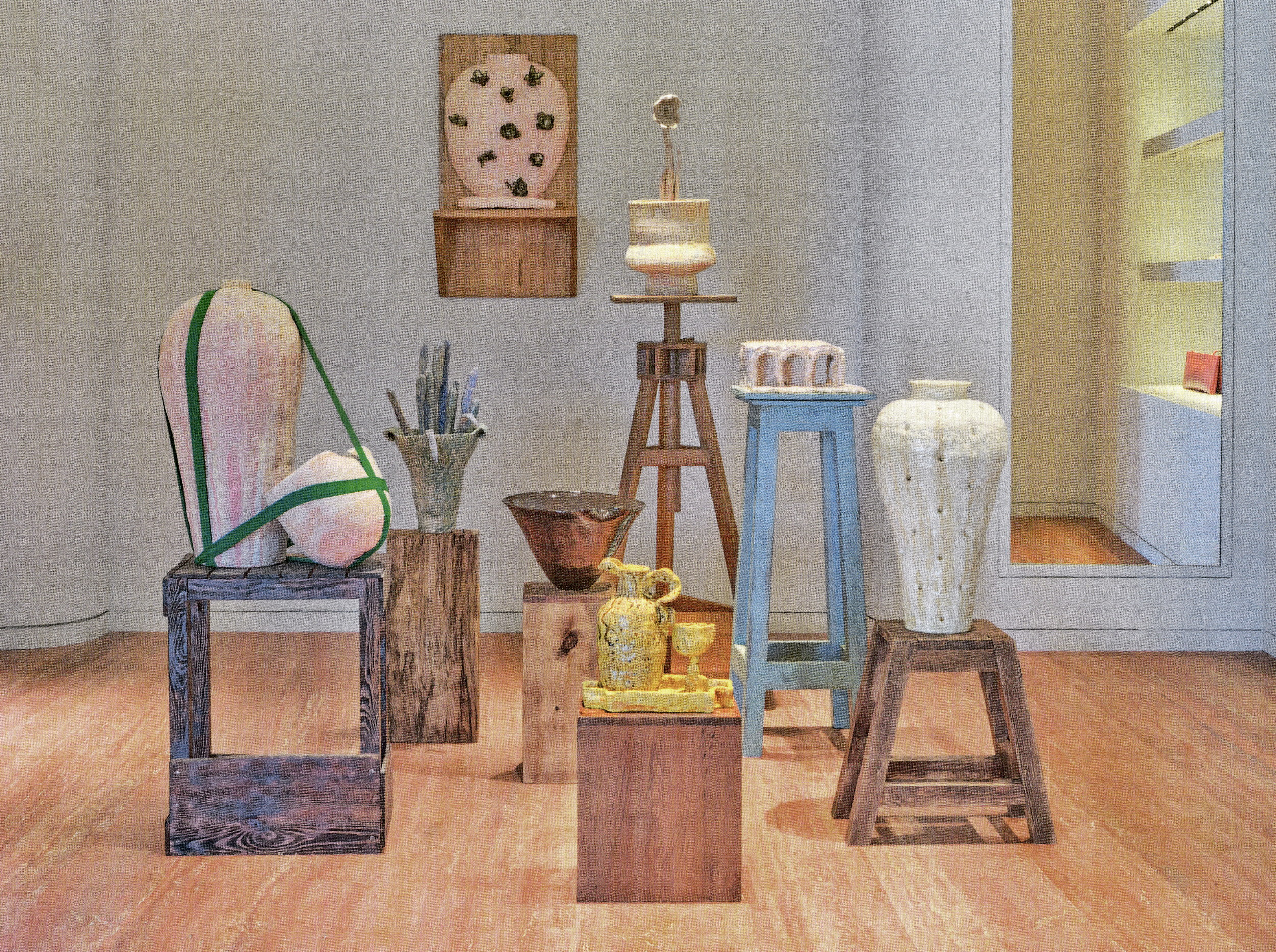 Une collection de sculptures et d'objets en céramique, dont des vases et des statues, exposés dans une pièce avec un sol en bois et un mur gris clair.