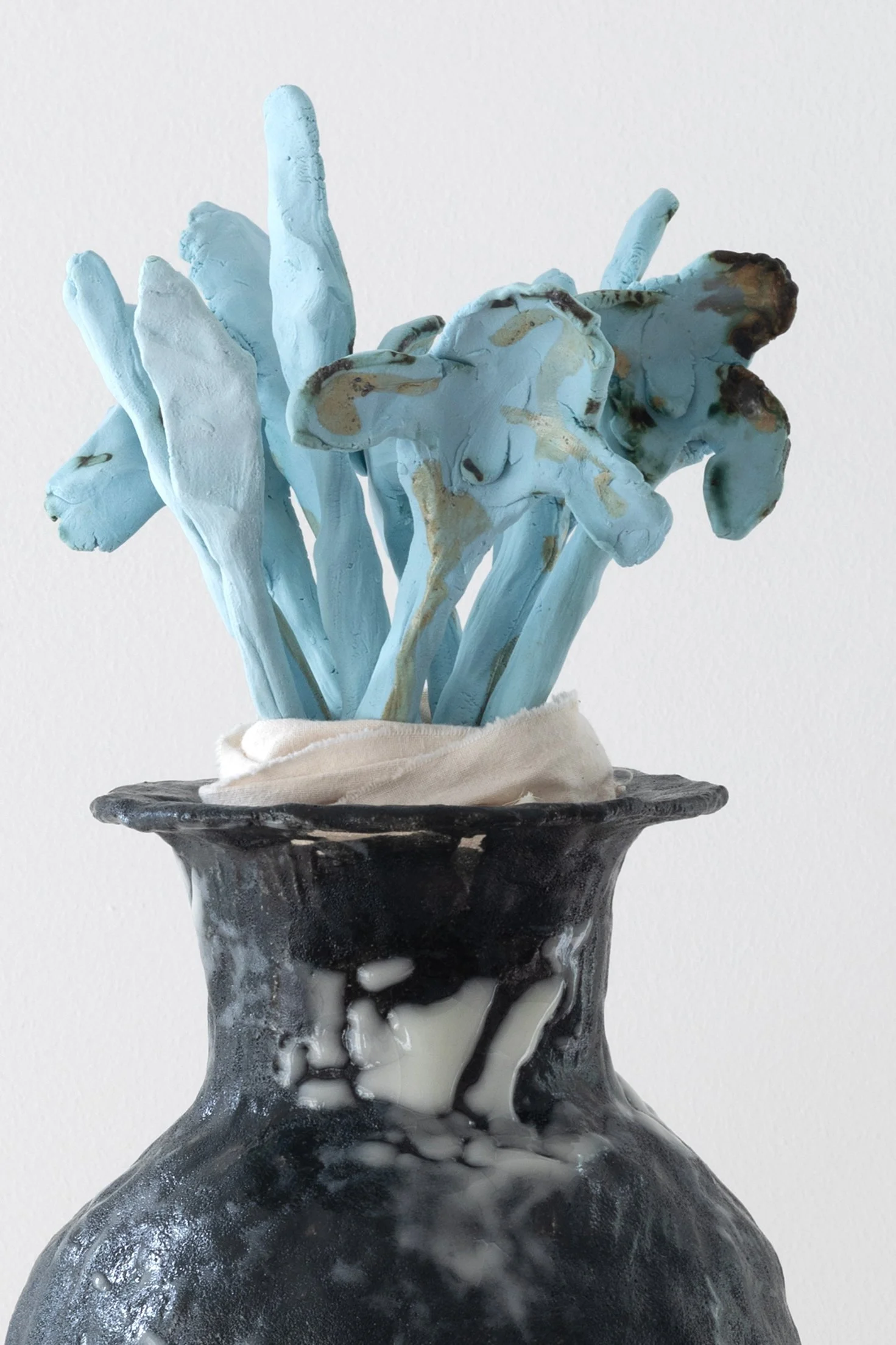 Une sculpture de fleurs peintes en bleu dans un vase noir et blanc avec un fond blanc.