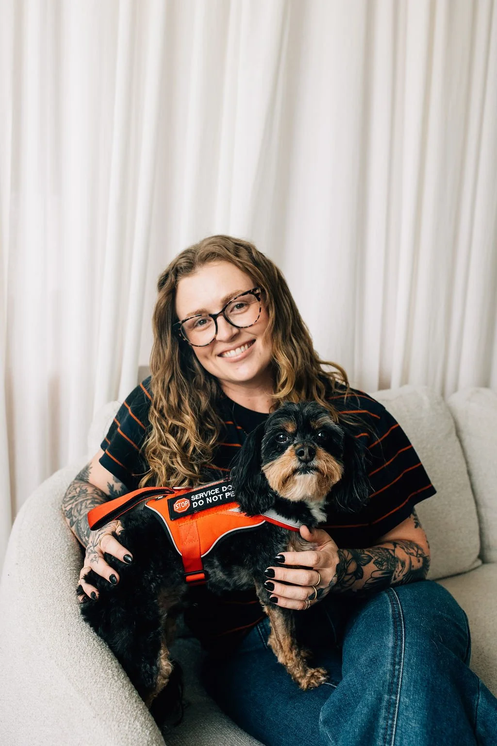 Colorado trauma therapist Chaucee sitting on a white couch with her small service dog named Jax