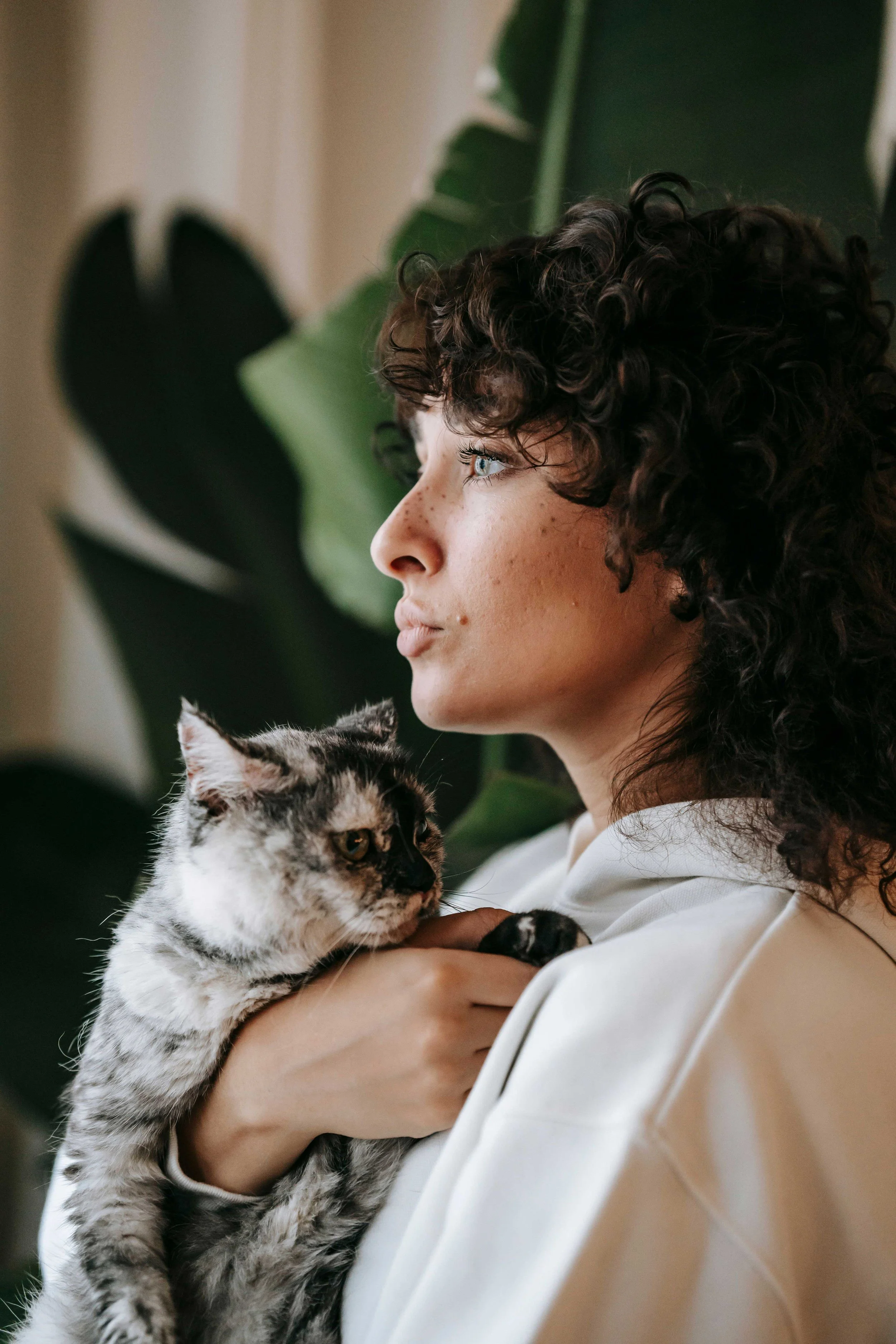 A young woman holding a black and white cat looking out the window