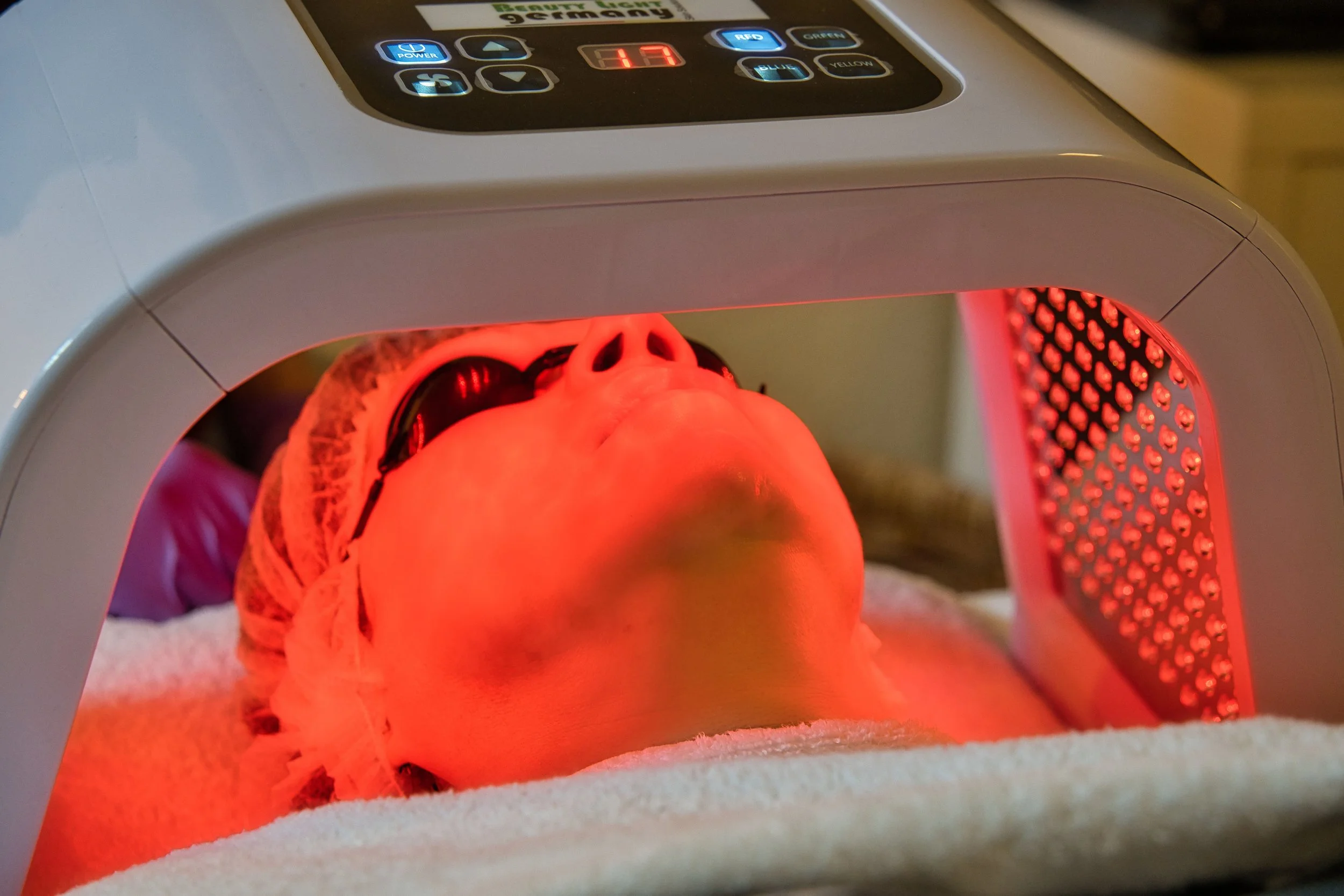 Eine Frau erhält eine Glow- & Anti-Aging-Behandlung im Kosmetikstudio Hautidee in Schwülper und liegt dafür mit dem Kopf und mit geschlossenen Augen unter rotem LED-Licht.