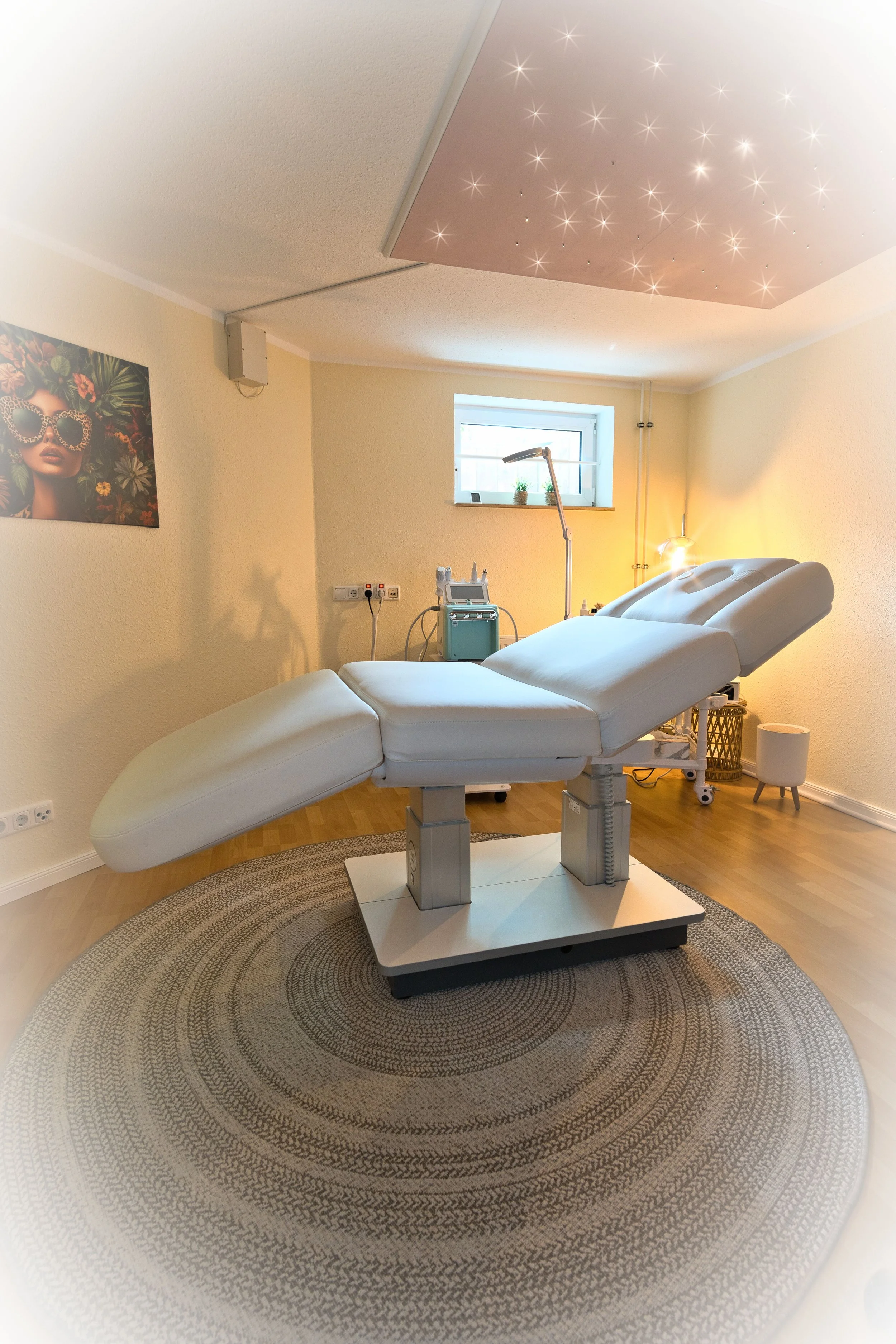 Das Kosmetikstudio Hautidee in Schwülper mit einer weißen Behandlungsliege, einem kleinen Fenster, einer Stehlampe und einem Bild an der Wand. Der Raum ist hell und freundlich gestaltet.
