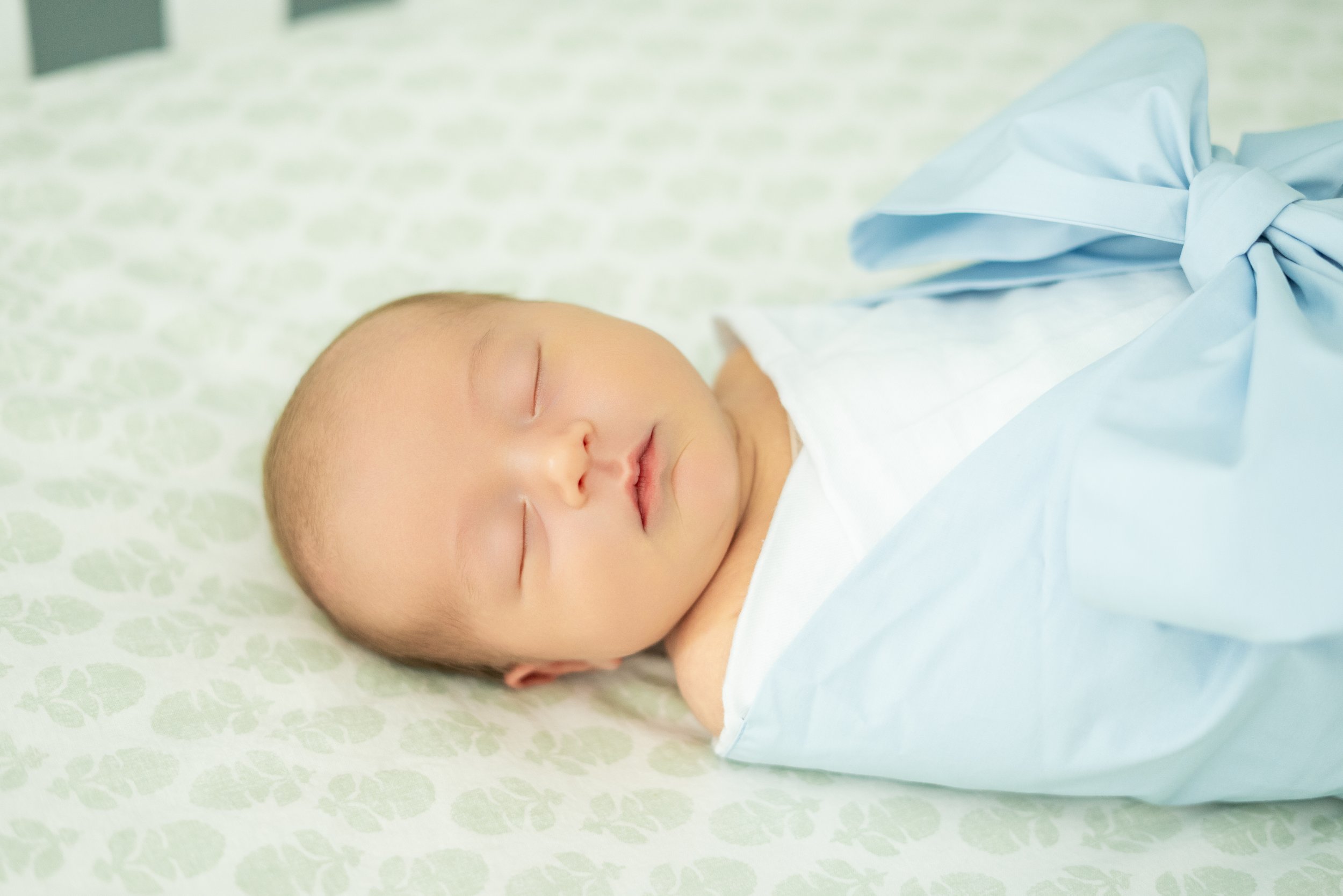 A sleeping baby with a peaceful expression lying on a patterned surface with a light blanket.