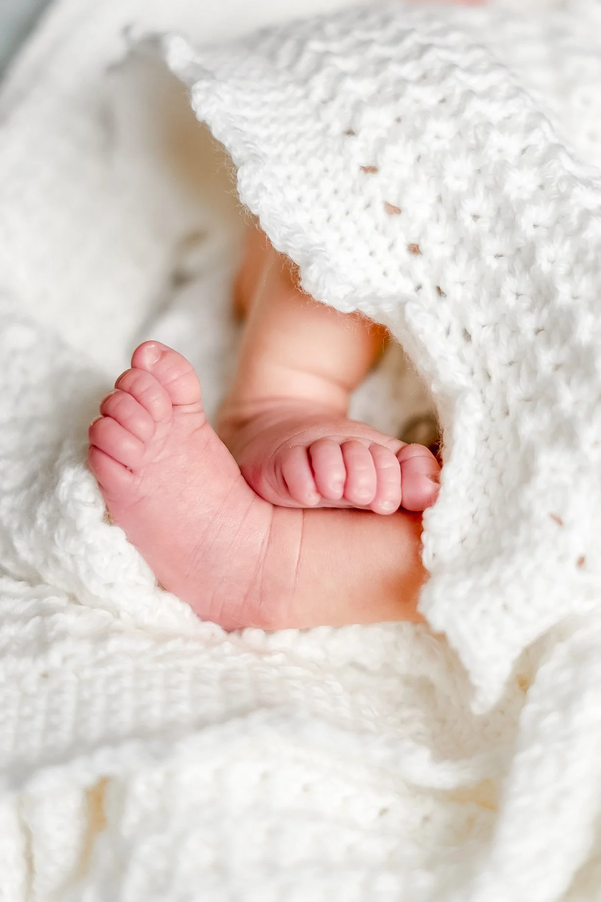 Close-up of a newborn baby's tiny feet resting on a soft, white, fuzzy blanket.