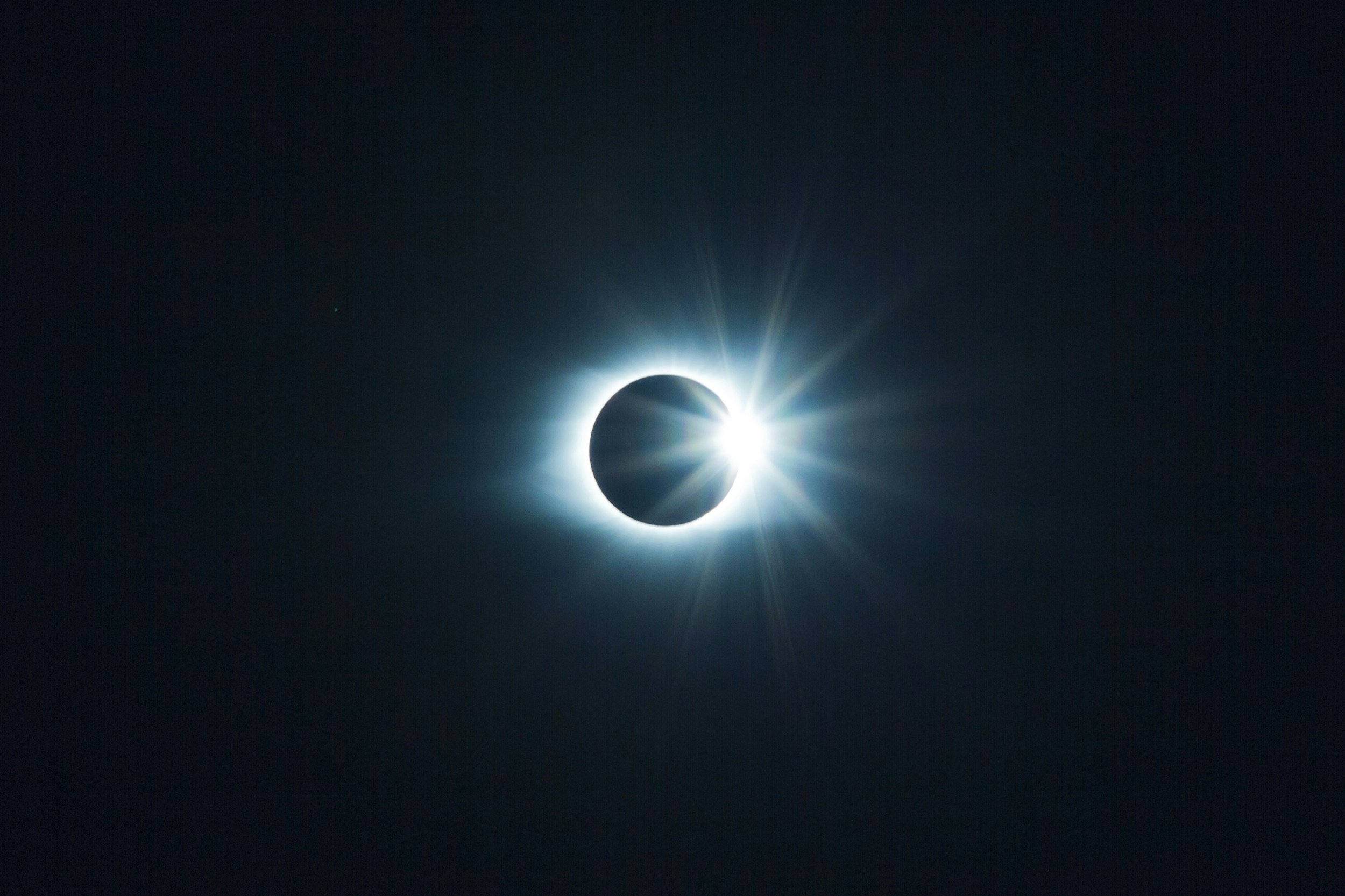 A solar eclipse with the moon covering the sun, revealing a bright corona and rays of light emanating from behind the moon.