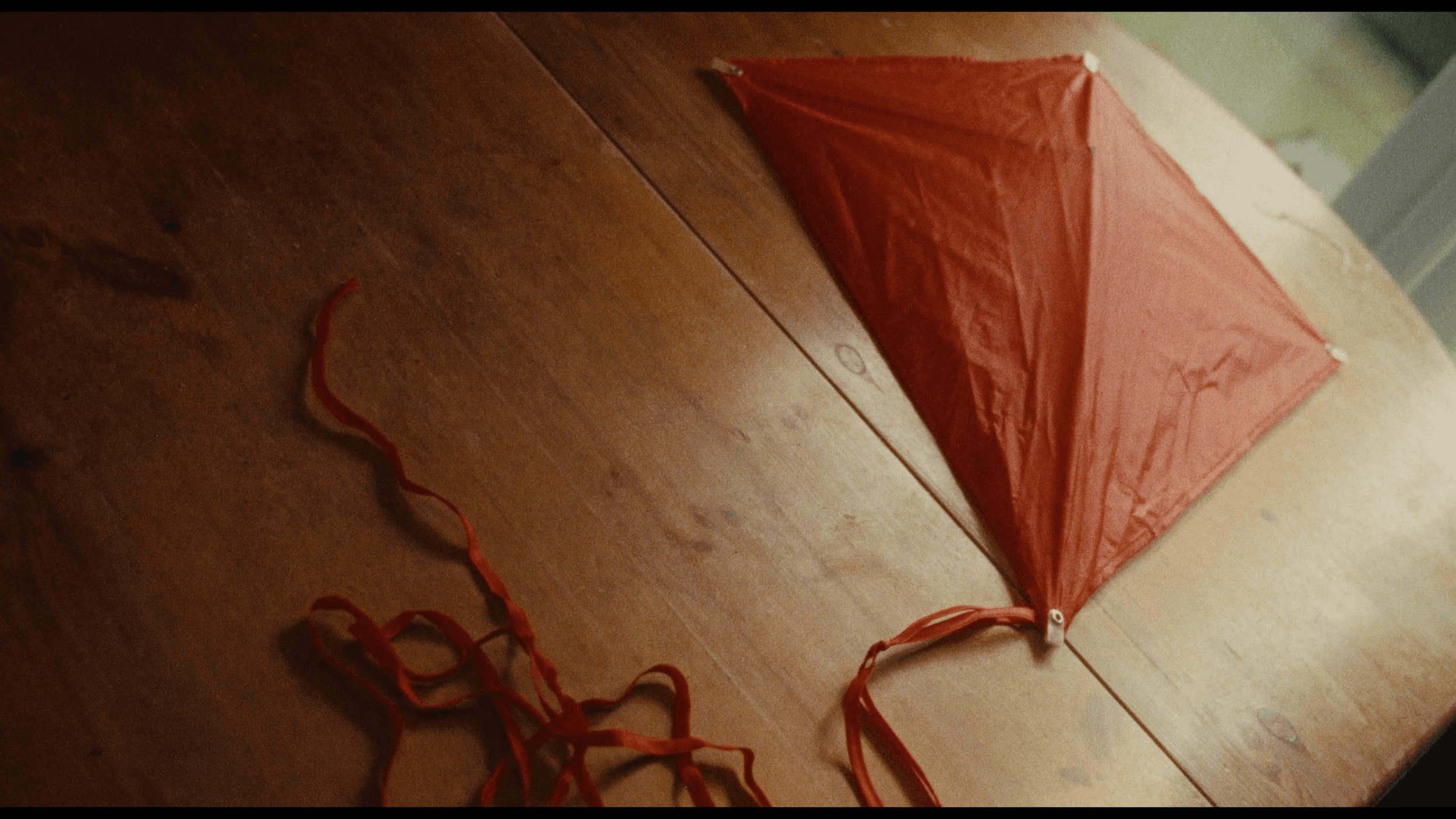 An orange and white kite lying on a wooden table with orange curly ribbons attached to it.