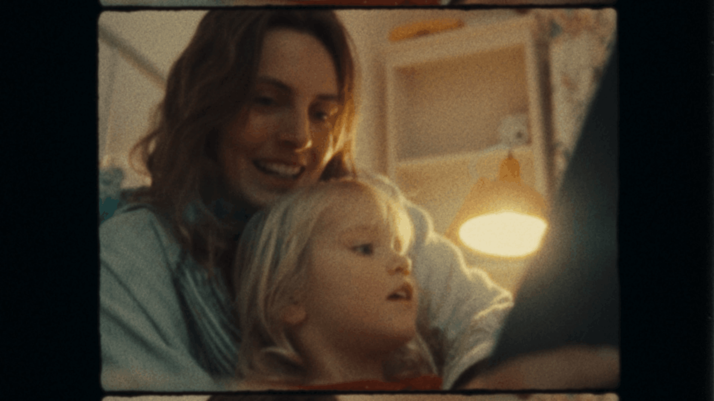A woman and a young girl looking at a tablet screen together, smiling in a cozy room with warm lighting.