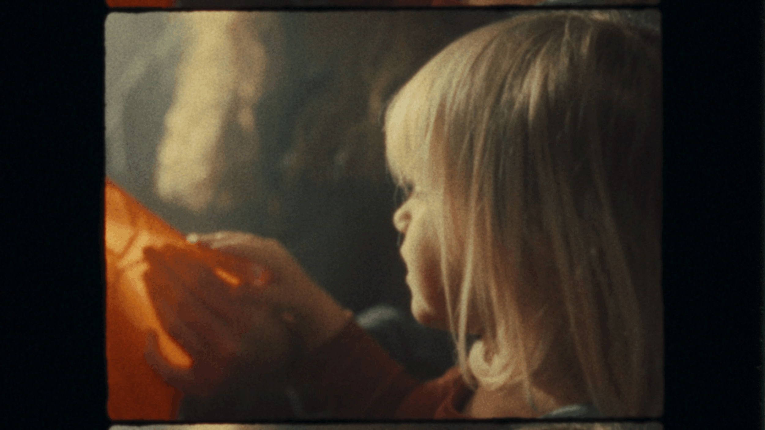 A person with blonde hair looking at an orange object, possibly a pumpkin