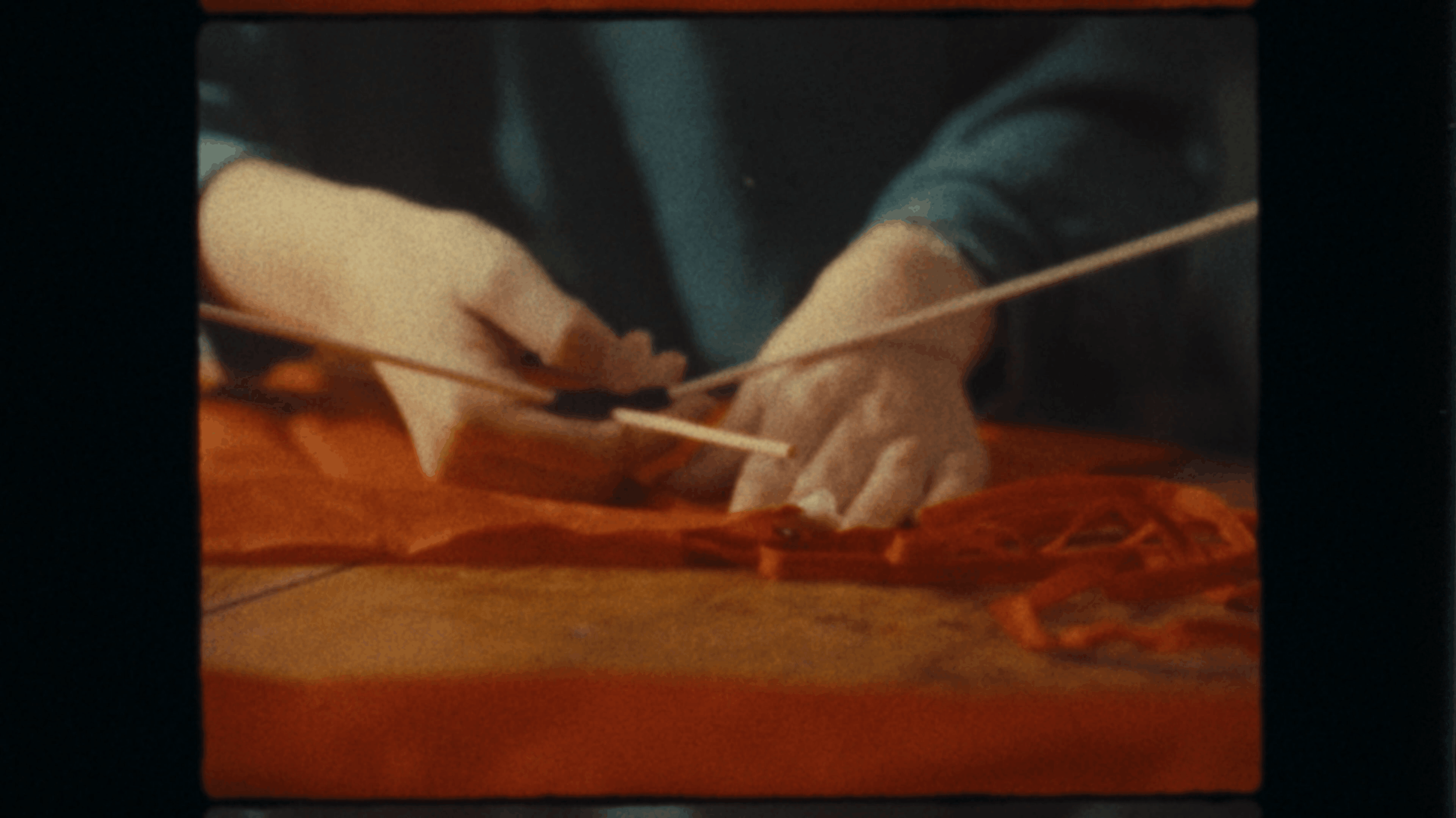 Close-up of hands arranging orange autumn leaves on a table, seen through a glass display case.