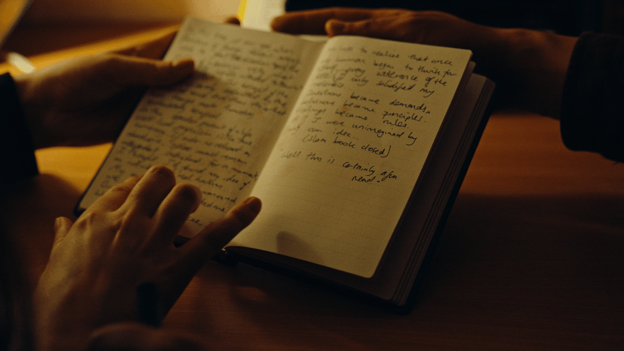 Close-up of a person flipping through a notebook with handwritten notes, illuminated by warm light.