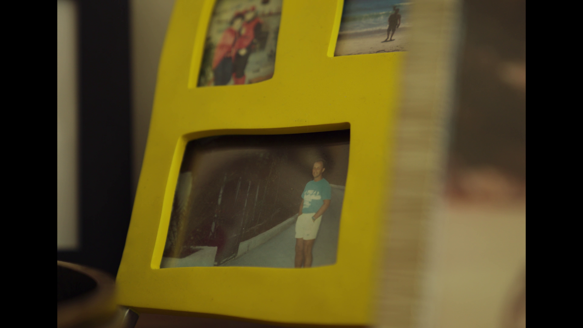 Yellow photo frame containing three photos, one of a man standing on a bridge, another of people in costumes, and a third of a person running on a beach.