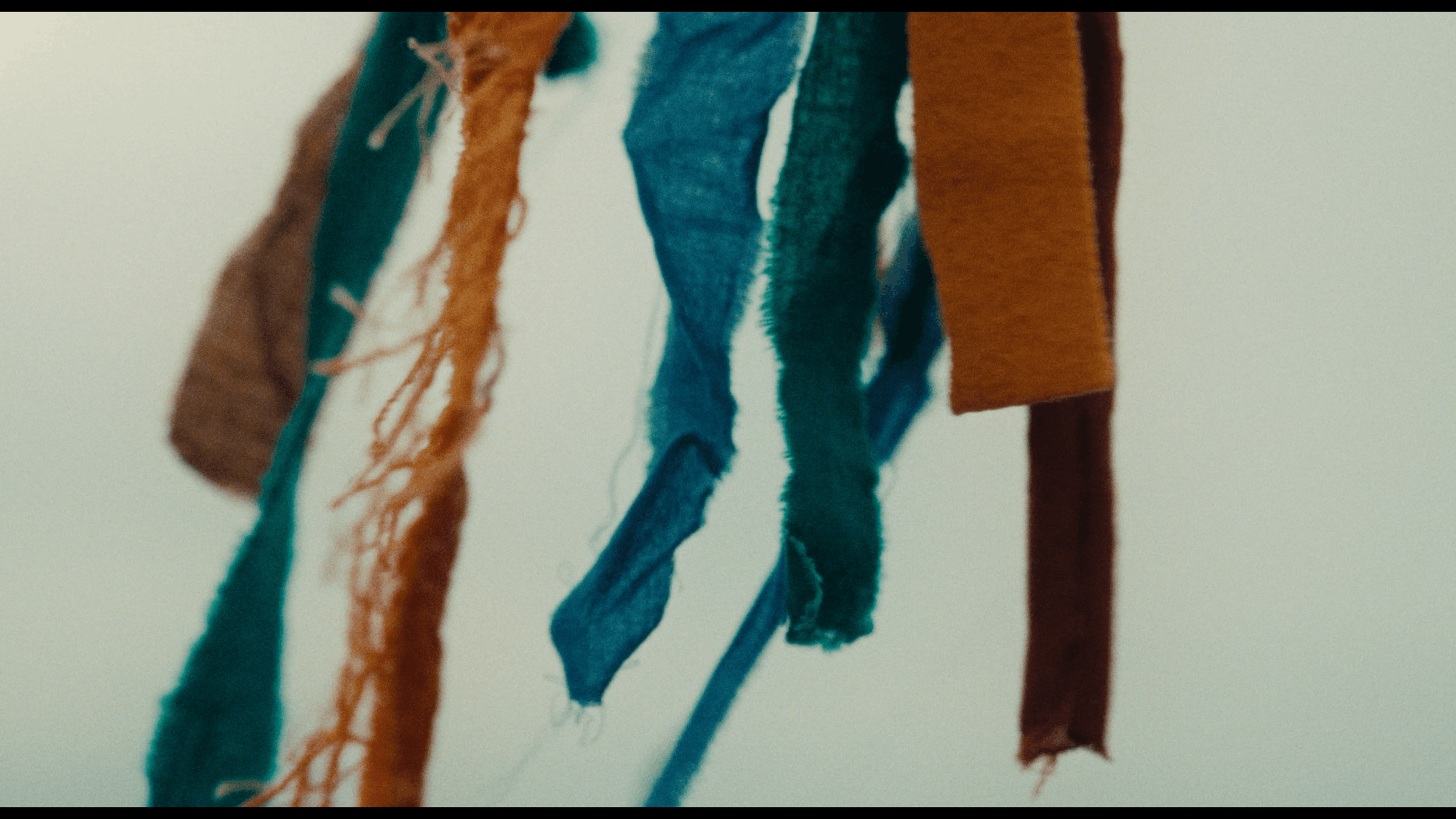 Close-up of a fabric sample with multiple colored fabrics hanging from a surface, including orange, teal, blue, and brown.