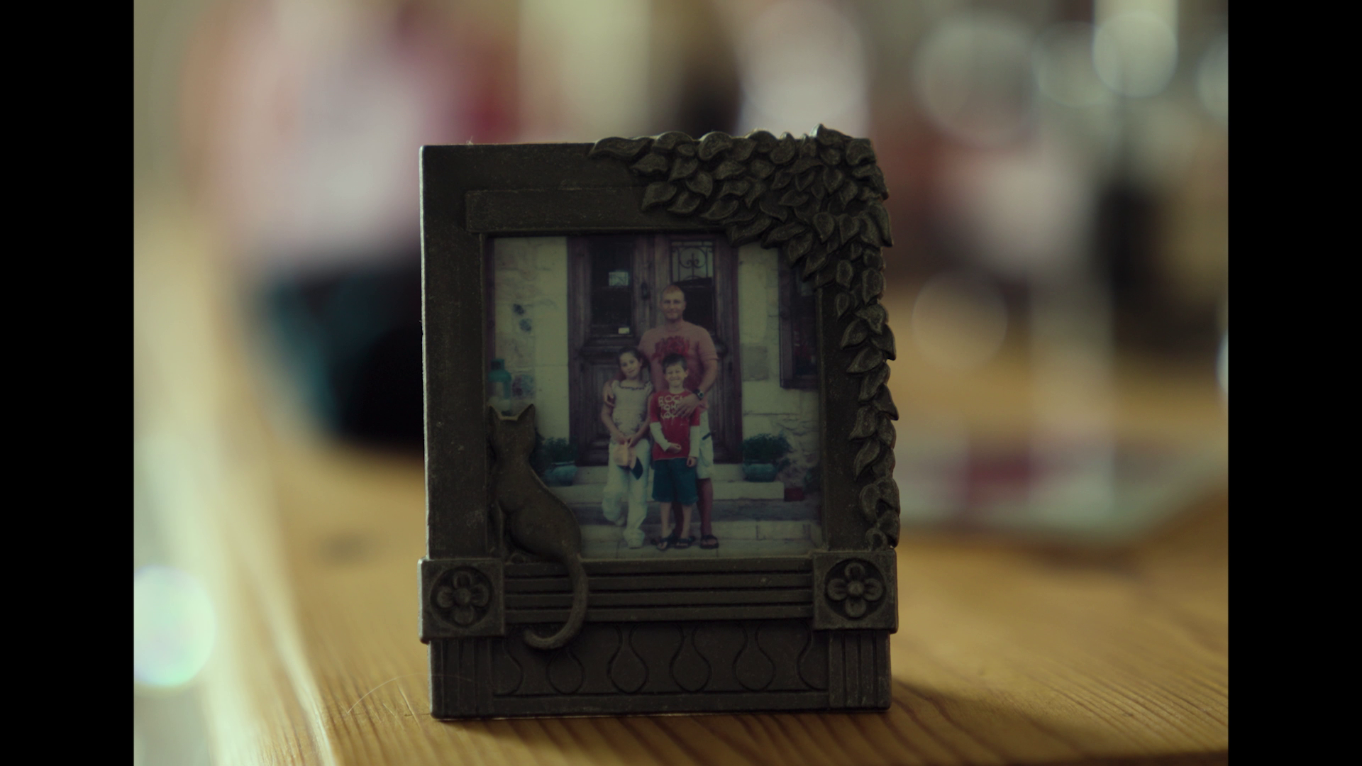A small decorative frame with a picture of a man and two children, adorned with a sunflower and a snail on it, standing on a wooden surface.