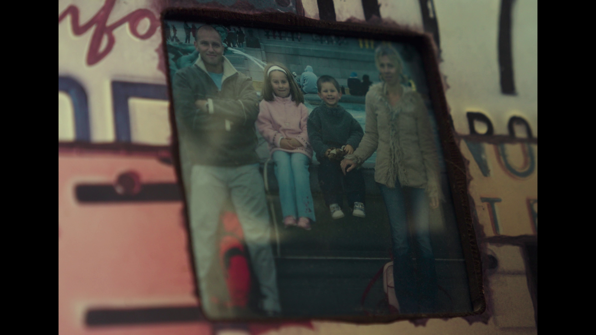 A framed photo of a man and three children outdoors, sitting and standing on a bench, with a city street background.