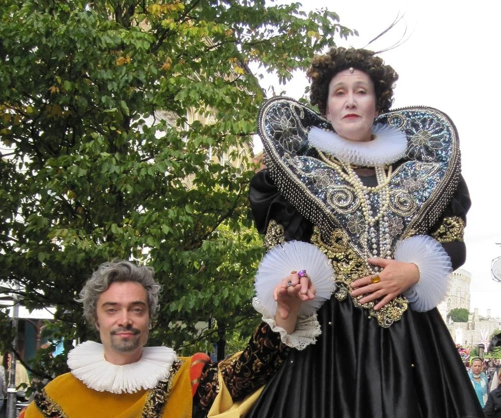 A man dressed as a Shakespearean character holding a woman in Elizabethan costume during a festival or parade.