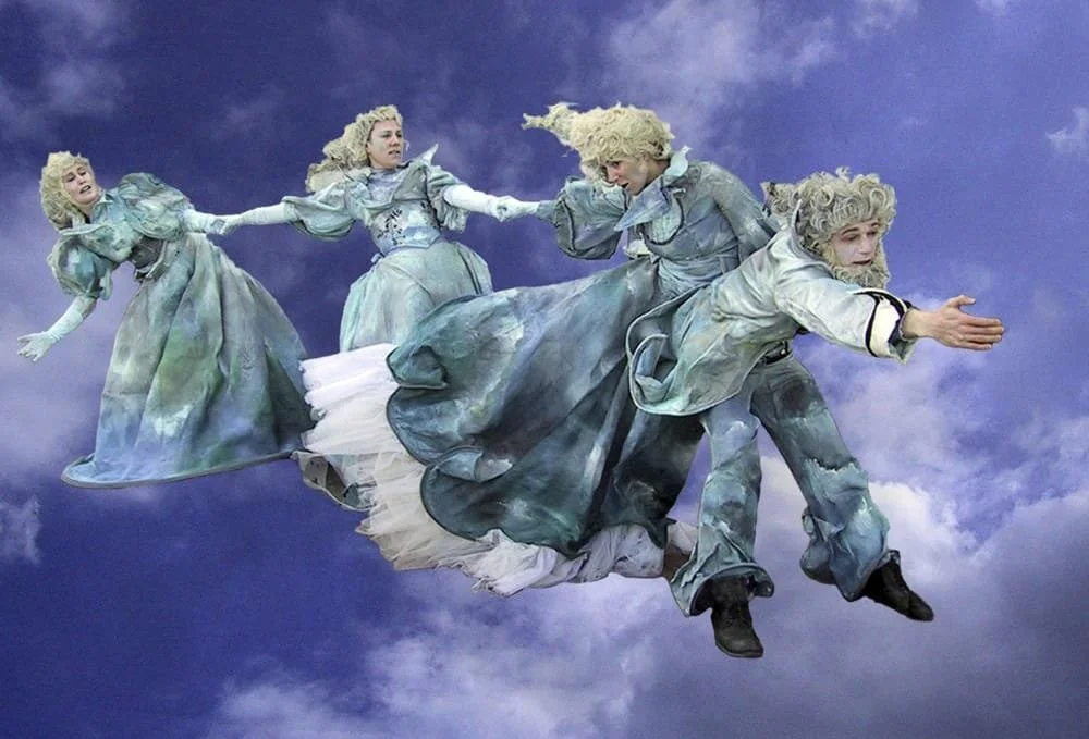 Four women in vintage dresses and wigs appear to be floating or flying against a cloudy sky background.