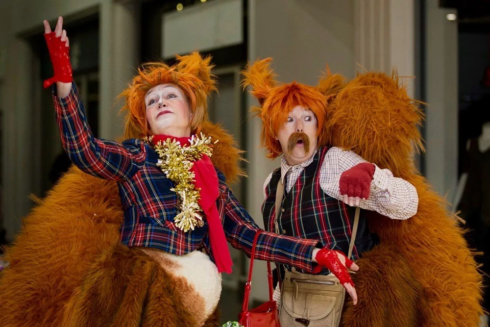 Two people dressed as lions and a woman in a plaid jacket and red gloves are taking a selfie at a festive event.