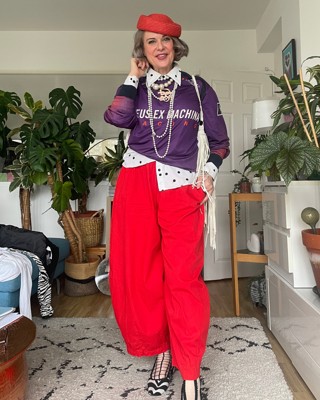 Creatively layered autumn outfit with jacket removed Jacket removed: purple sweatshirt becomes the top layer over polka dot shirt, with pearls, red pillbox beret and red balloon trousers.