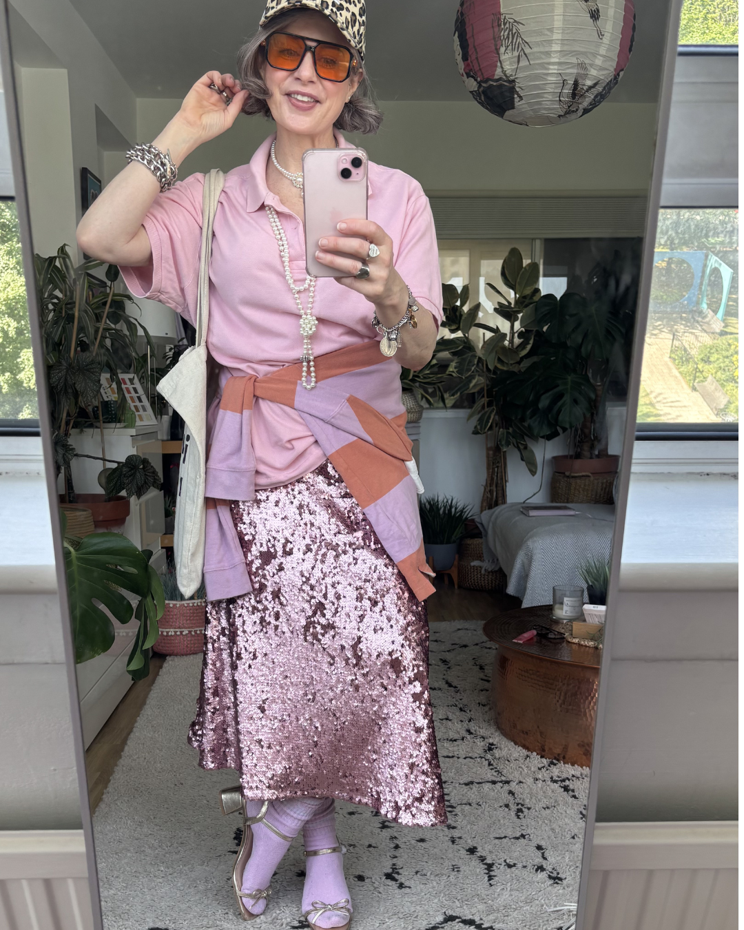 Pink sequin skirt outfit over 40 — pink polo shirt, sweatshirt tied at waist, leopard cap, gold Mary Janes, pearl necklace — style diary women over 40