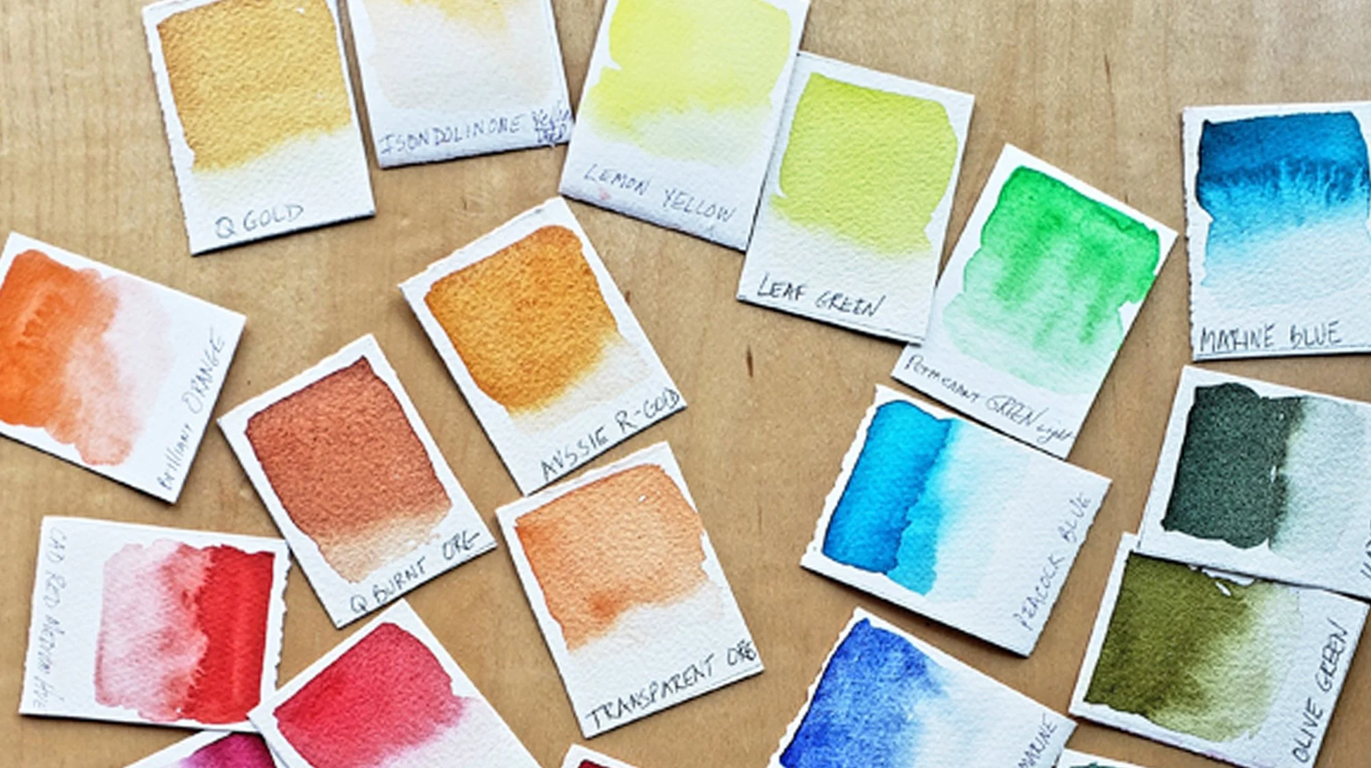 Collection of small watercolor paint swatches in various colors including gold, yellow, green, blue, and orange with handwritten labels. Painted by Lorraine Rimmelin.