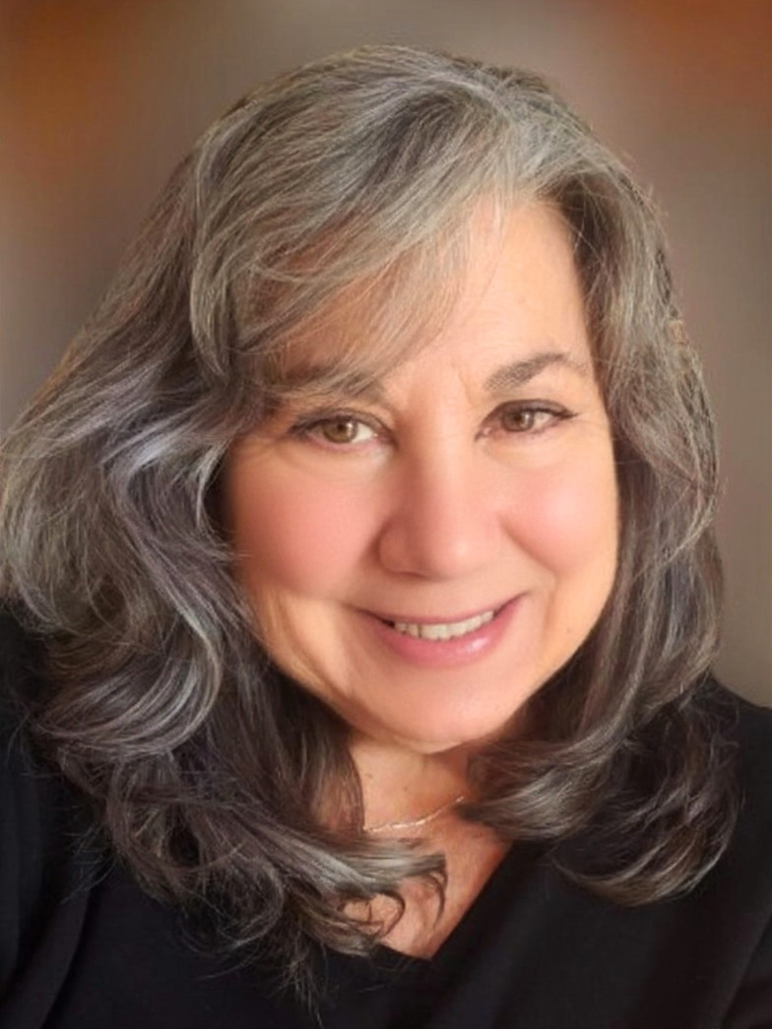 Lorraine Rimmelin, watercolor artist and teacher, with gray, wavy hair and light skin smiling, wearing a black top