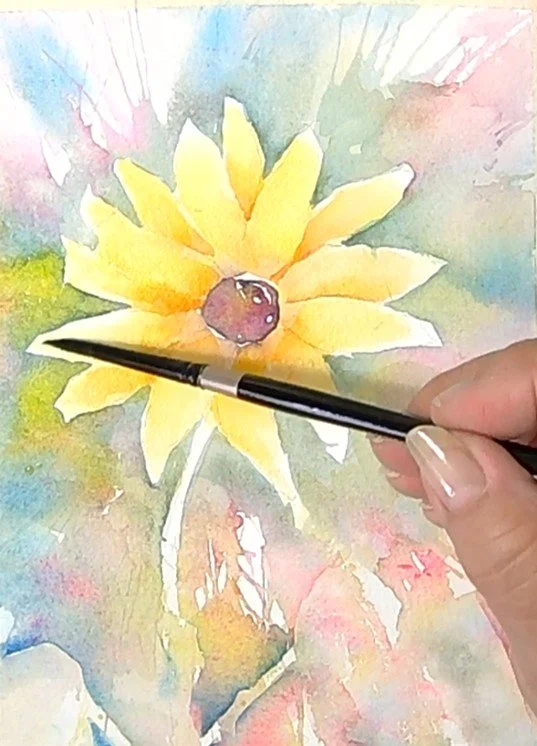Close-up of a hand holding a paintbrush, painting a watercolor floral artwork featuring a yellow flower with a brown center and a green stem. Painted by Lorraine Rimmelin.