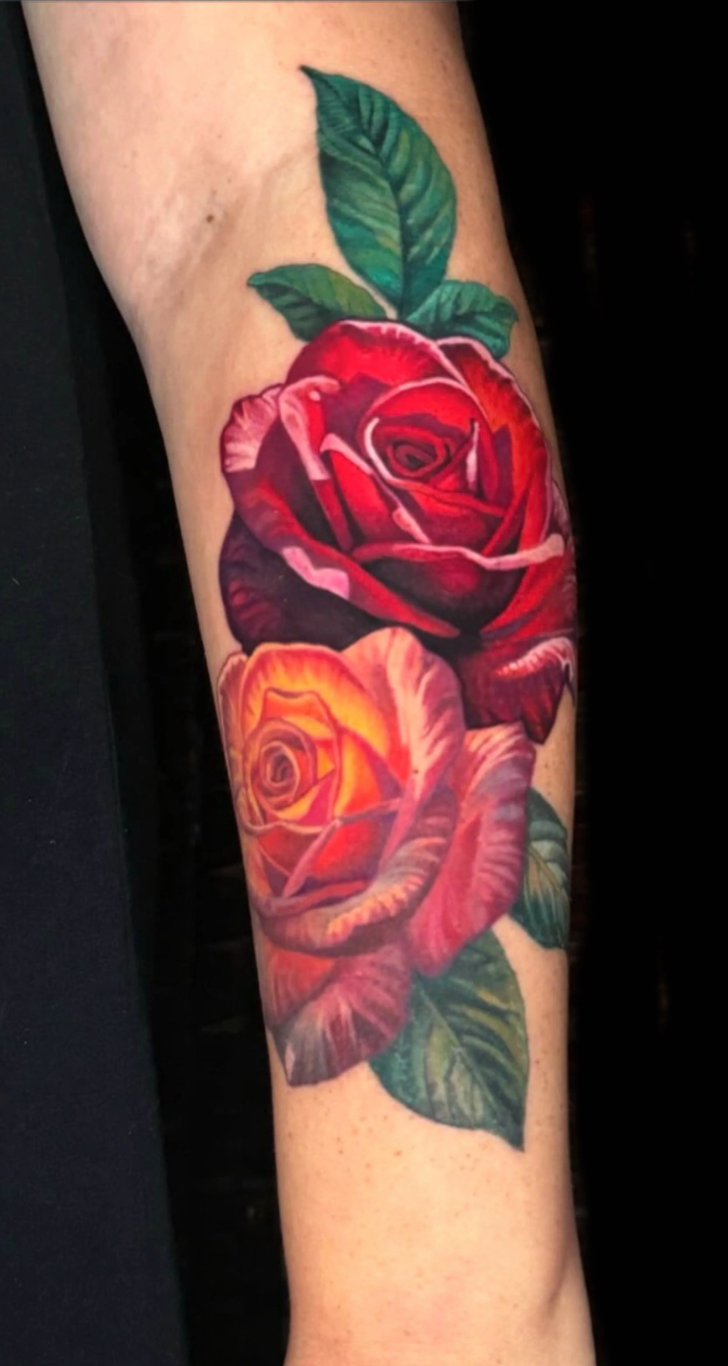 Vibrant red and orange rose tattoo on the arm