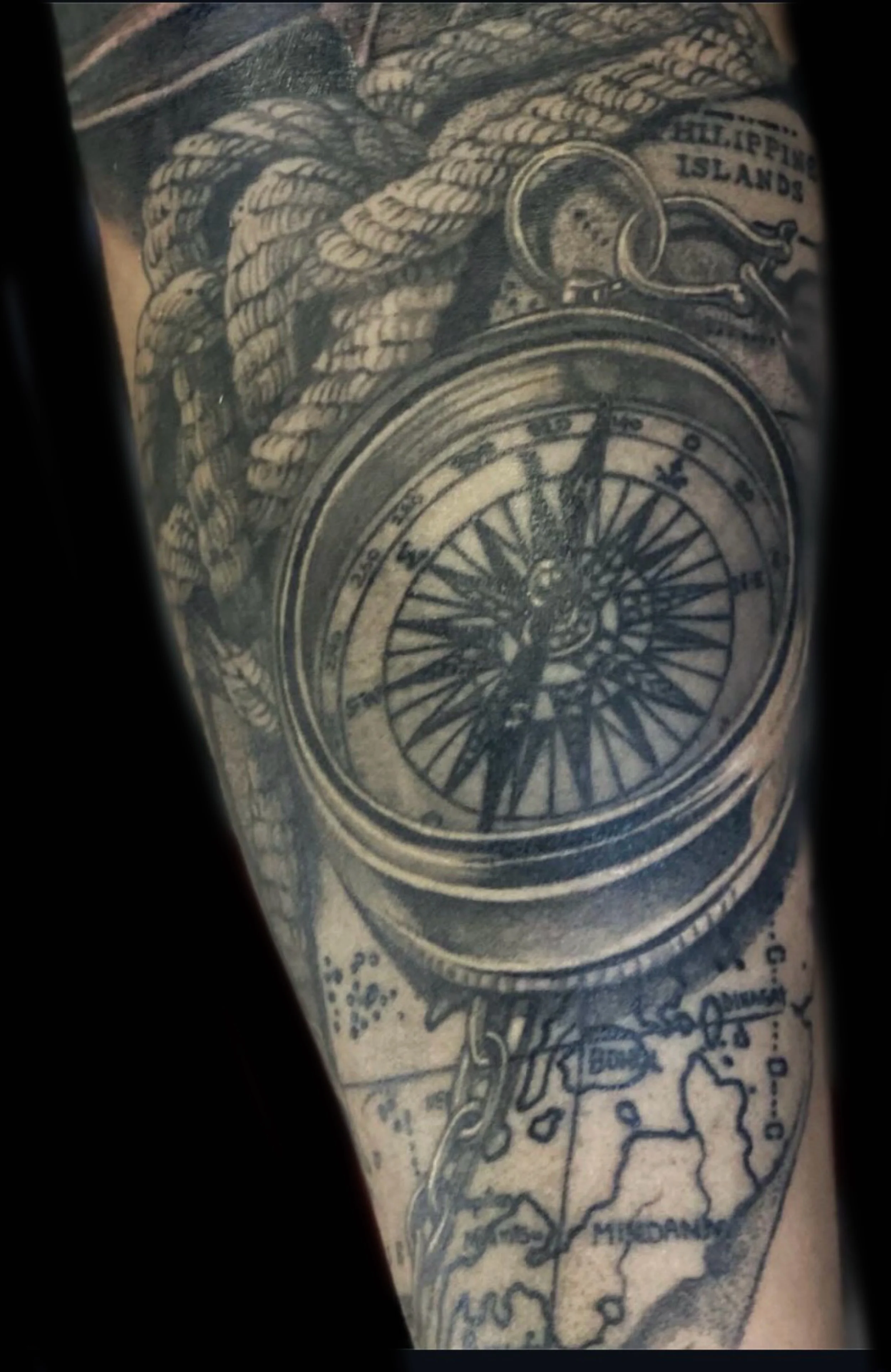 Black and grey compass tattoo over a detailed map design
