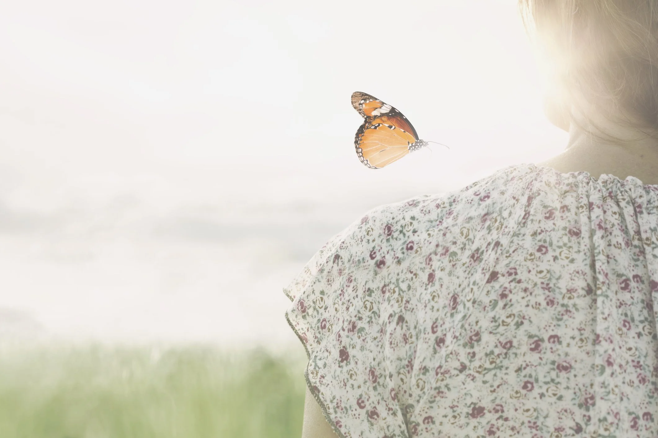Child with a butterfly resting on their arm in soft natural light.