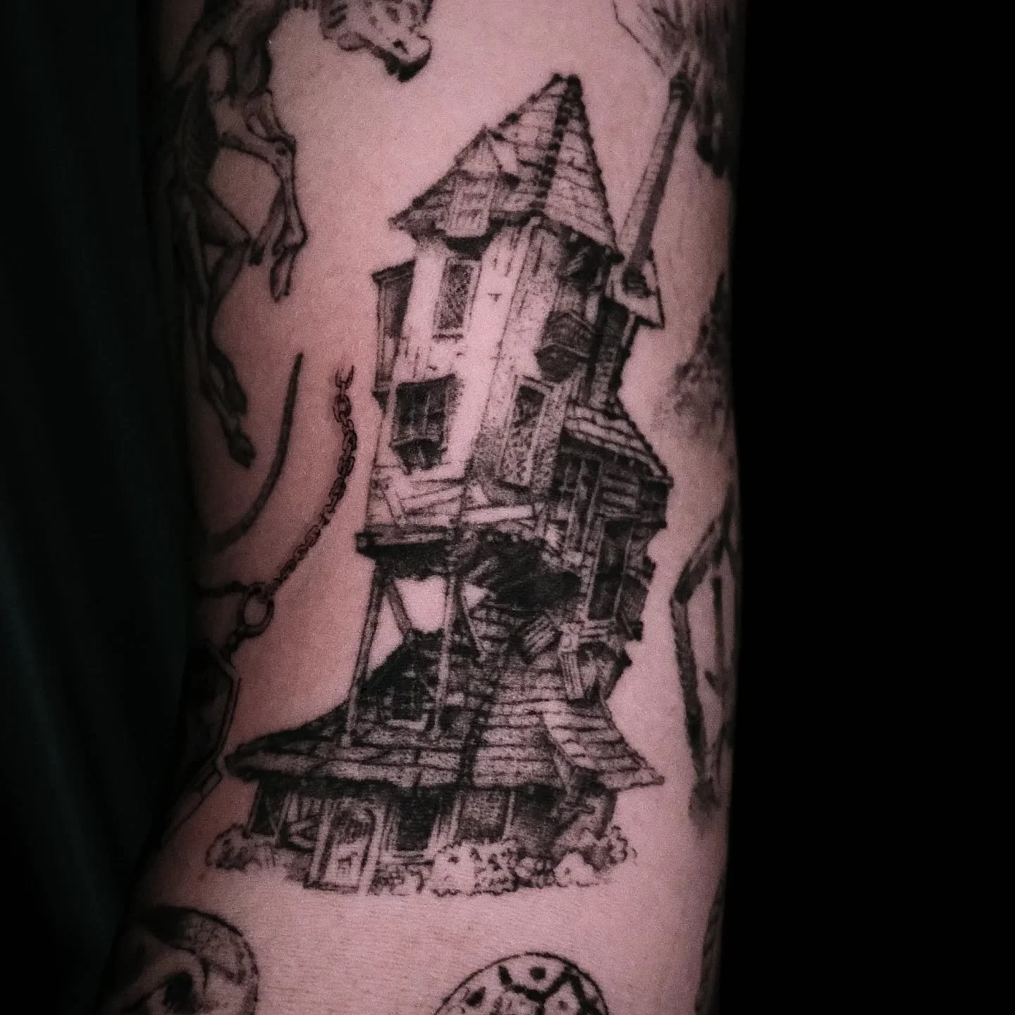 Tattoo of a detailed black and gray illustration of the Weasleys house from Harry Potter on a person's arm.