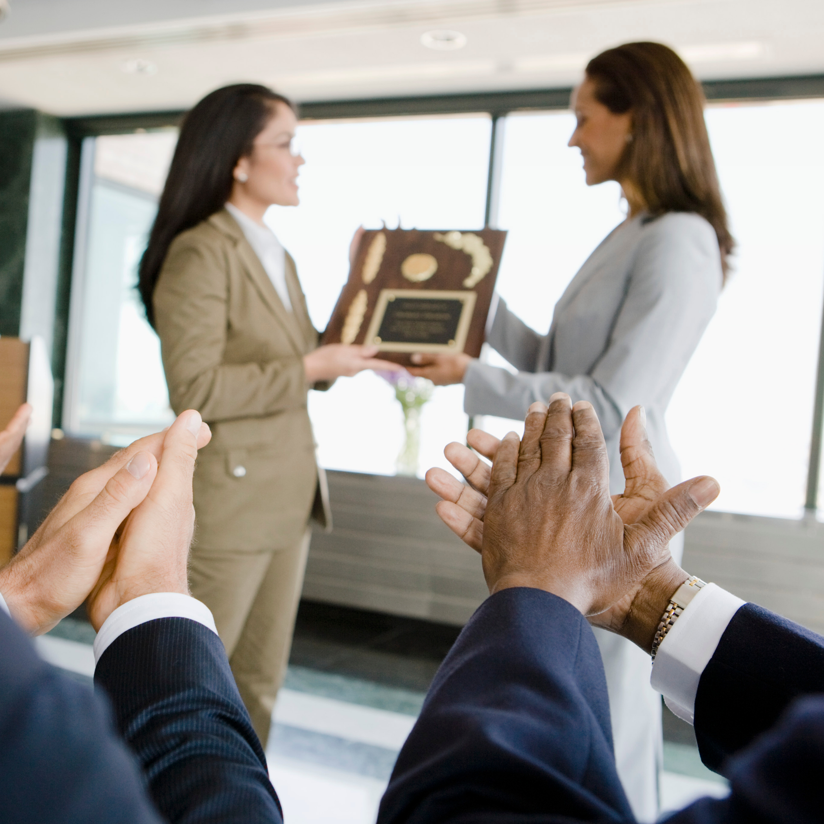 People applauding as one person presents an award plaque to another during a ceremony.